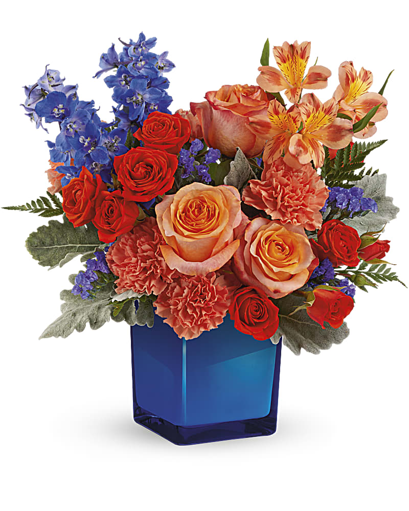 Teleflora's Blue Daydream Bouquet - A dream come true in orange and blue! Bold orange roses in a cobalt glass cube make any day memorable. Orange roses, dark orange spray roses, orange alstroemeria, orange carnations, blue delphinium and blue sinuata statice are arranged with dusty miller and leatherleaf fern. Delivered in a Color Splash Cube.