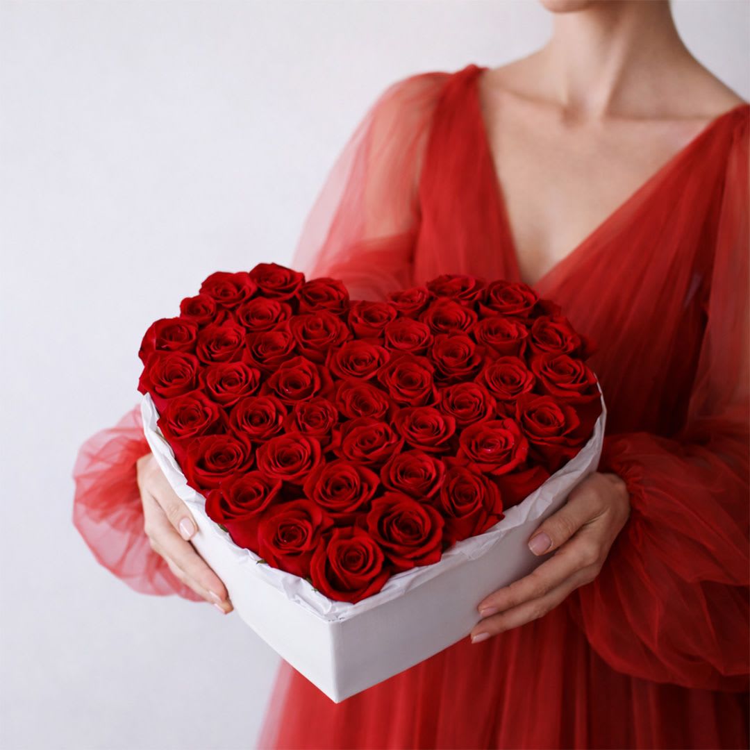 Heart-shaped box of red roses held by a woman in a red dress