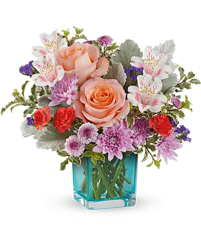 Teleflora's Enchanting Garden Bouquet - Step into enchantment with this delightful turquoise glass cube, showcasing vibrant and colorful blooms inspired by the beauty of a blooming garden. Uncover floral elegance with a garden-inspired bouquet of peach roses, pink alstroemeria, orange carnations, lavender chrysanthemums, purple sinuata statice, and accents of dusty miller and pitta negra. Presented in the Turquoise Cube, this Enchanting Garden Bouquet radiates charm and sophistication.