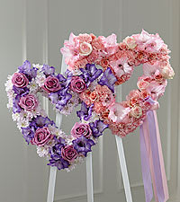 Double Hearts on an Easle Easel - Pay tribute to a love that not even death can diminish. This creative and eloquent statement of everlasting romance is expressed by a pair of floral hearts, beautifully entwined.  this poetic masterpiece of sympathy is designed to be displayed on a wooden stand at a wake, a funeral service, or a graveside burial service. It includes pink carnations, roses and gladiolus, lavender cushion pompons and roses and purple gladiolus ... a very personal and loving tribute to the memory of one who was extravagantly loved