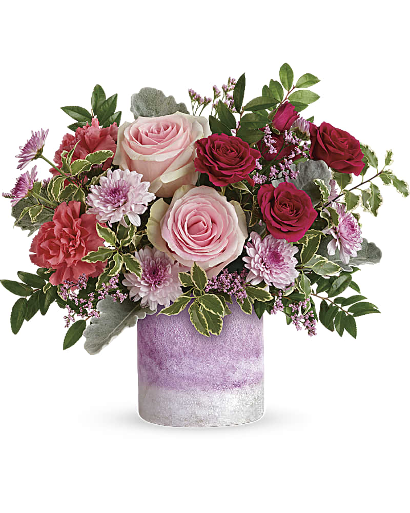 Teleflora's Washed In Pink Bouquet - When you want to make them feel extra special, think pink! This pretty present of pink roses and lavender blooms is arranged in a hand-blown, art-glass vase with frosted finish and the prettiest shade of pink. Pink roses, dark pink spray roses, pink carnations, lavender cushion spray chrysanthemums and lavender limonium are arranged with dusty miller, huckleberry and pitta negra. Delivered in an Orchid Color Frost Art Glass cylinder.