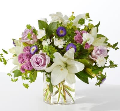 April Showers Bouquet - Soft, serene, and effortlessly elegant, this bouquet brings a sense of calm beauty to any space. Lavender roses pair with white lilies for a touch of timeless grace, while purple asters and pink mums add gentle color and texture. Delicate white blooms and lush greenery complete the design, creating a fresh, airy arrangement that feels both comforting and refined. Presented in a clear glass vase, it’s the perfect choice for celebrating life’s tender moments, offering sympathy, or simply brightening someone’s day with a peaceful touch.