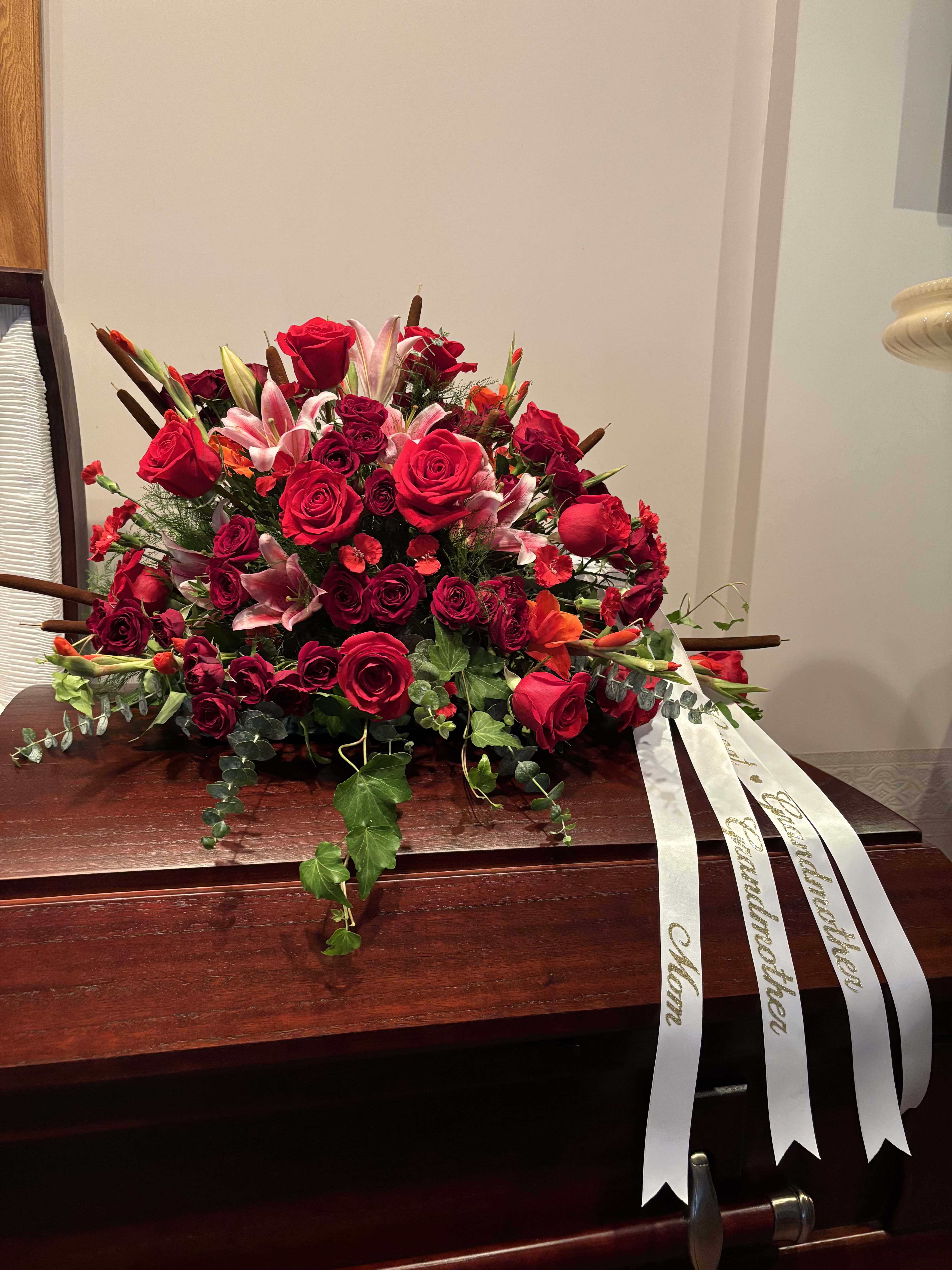 Crimson Casket Spray - Rich tones of red roses and gladioluses, highlighted with stargazer lilies and unique trailing greens.