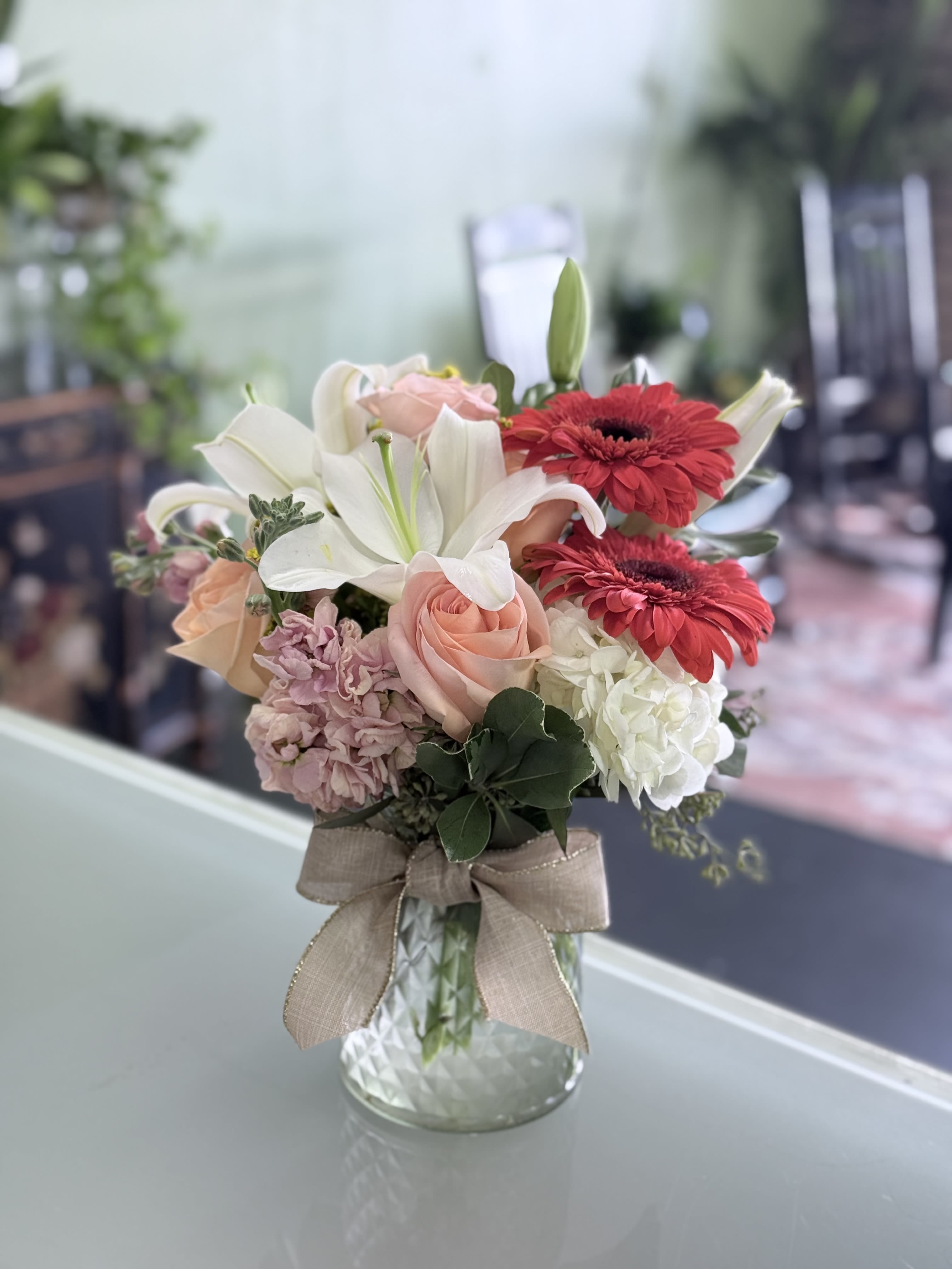 Bouquet of lilies, roses, and gerbera daisies in a glass vase with a ribbon