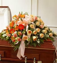 Peach Garden Tribute - A half casket spray featuring soft and elegant peach tones.  This graceful tribute is designed with peach roses and peach gerbera daisies, beautifully complemented by assorted peach blooms and lush fresh greenery. A delicate peach ribbon bow adds a gentle finishing touch, creating a warm and comforting display of love and remembrance. The arrangement rests across half of the casket and is thoughtfully crafted to honor a cherished life with softness, beauty, and serenity.