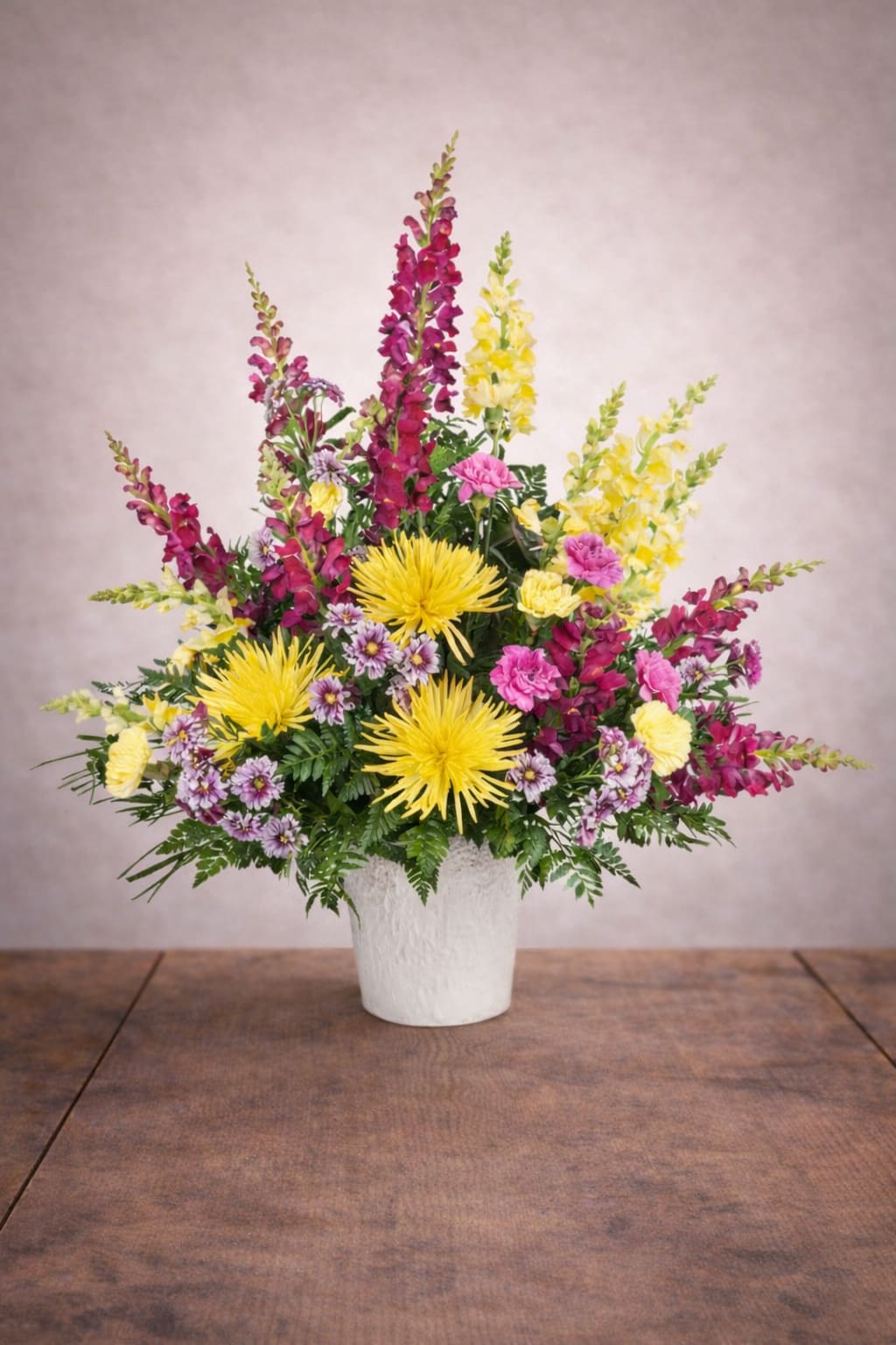 Warm Remembrance Sympathy Arrangement - Warm Remembrance Sympathy Arrangement is a vibrant sympathy flower arrangement designed to celebrate a life beautifully lived. This uplifting design features bright yellow spider mums, colorful snapdragons in shades of burgundy and soft yellow, delicate pink carnations, and charming daisy poms arranged among lush greenery. The cheerful palette of yellow, pink, and rich magenta creates a warm and comforting tribute that honors cherished memories while bringing a sense of hope and light.  Expertly designed by the floral artists at Floral Fabulous, a trusted local florist in Round Rock TX near Austin, this arrangement is perfect for celebration-of-life services, memorial gatherings, or sending heartfelt condolences to family and friends. Tall snapdragons add graceful height and elegance while spider mums create a bold focal point surrounded by soft carnations and delicate accent flowers.  Each arrangement is handcrafted using fresh premium blooms to ensure a meaningful and beautiful tribute. Floral Fabulous proudly offers dependable flower delivery in Round Rock, Pflugerville, Georgetown, and surrounding Austin communities.  Warm Remembrance is a thoughtful way to celebrate a loved one’s life while offering comfort, support, and lasting remembrance.
