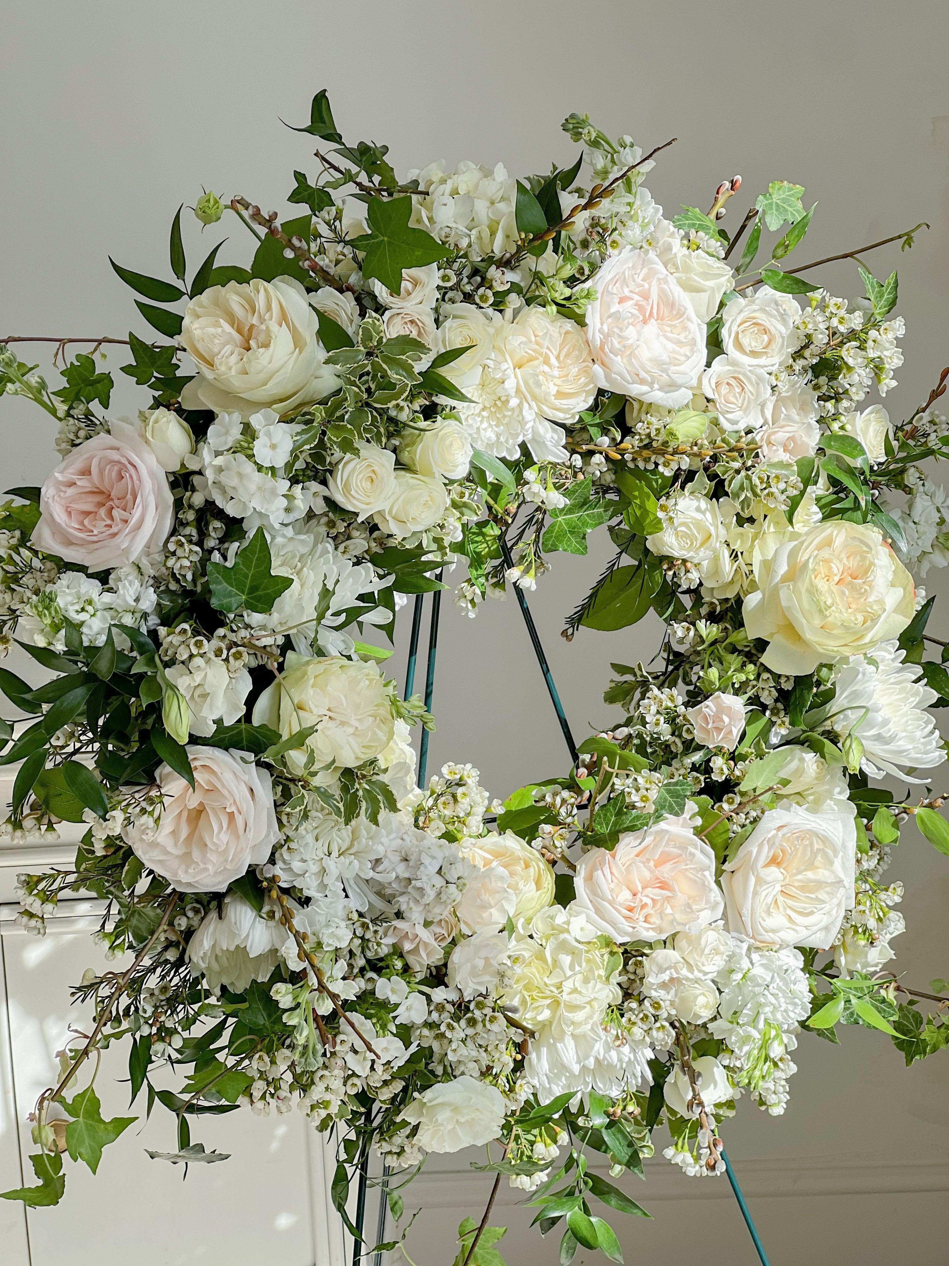 Sympathy Wreath  - Our designer will include fresh seasonal blooms to match the design in the picture, the overall colors are light and neutral.  The wreath will come with on a standing easel.   *If you'd like to further customize your order, please give us a call and we can place your order via phone.  *Please note that the images are for reference only. Our selection of flowers is always changing to ensure a fresh, seasonal mix of blooms. We cannot guarantee specific varieties and we will try to accommodate special requests.