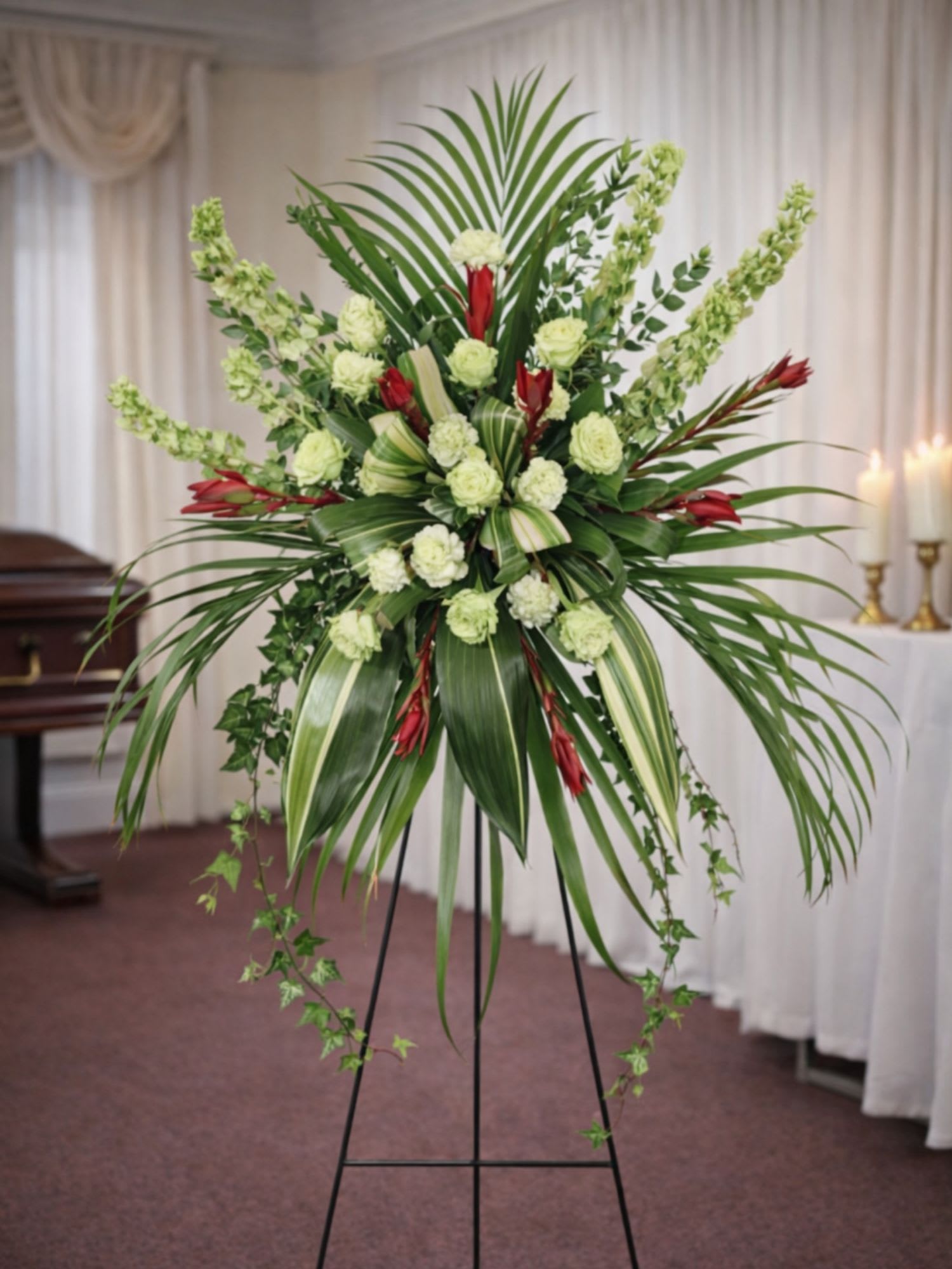 Final Flight Standing Spray  - Final Flight Standing Spray is a striking and modern sympathy tribute designed to honor a loved one with elegance and dignity. This dramatic standing spray features soft green roses, delicate green carnations, fresh snapdragons, and vibrant red tropical accent flowers arranged among sweeping palm leaves and cascading greenery. The bold tropical foliage creates a graceful wing-like shape that symbolizes a peaceful final journey and lasting remembrance.  Expertly designed by the floral artists at Floral Fabulous, a trusted local florist in Round Rock TX near Austin, this standing spray offers a contemporary and meaningful tribute for funeral services, memorial ceremonies, and celebration-of-life gatherings. The soft green palette represents renewal and peace, while the rich red tropical blooms add warmth and heartfelt admiration.  Displayed on a standing easel, the Final Flight Standing Spray creates a powerful and elegant presence during memorial services. Each arrangement is handcrafted with fresh premium flowers to ensure a beautiful tribute that reflects love, remembrance, and honor.  Floral Fabulous proudly offers professional funeral flower delivery in Round Rock, Pflugerville, Georgetown, and throughout the greater Austin Texas area.  Final Flight Standing Spray is a thoughtful way to celebrate a life, express sympathy, and honor cherished memories with a graceful and modern floral tribute.