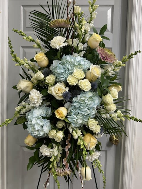 Touch of Blooms  Standing Spray - Light Blue Hydrangea, White Roses, Light Yellow Roses, Snapdragons, Stock, Carnations, Fancy Greens