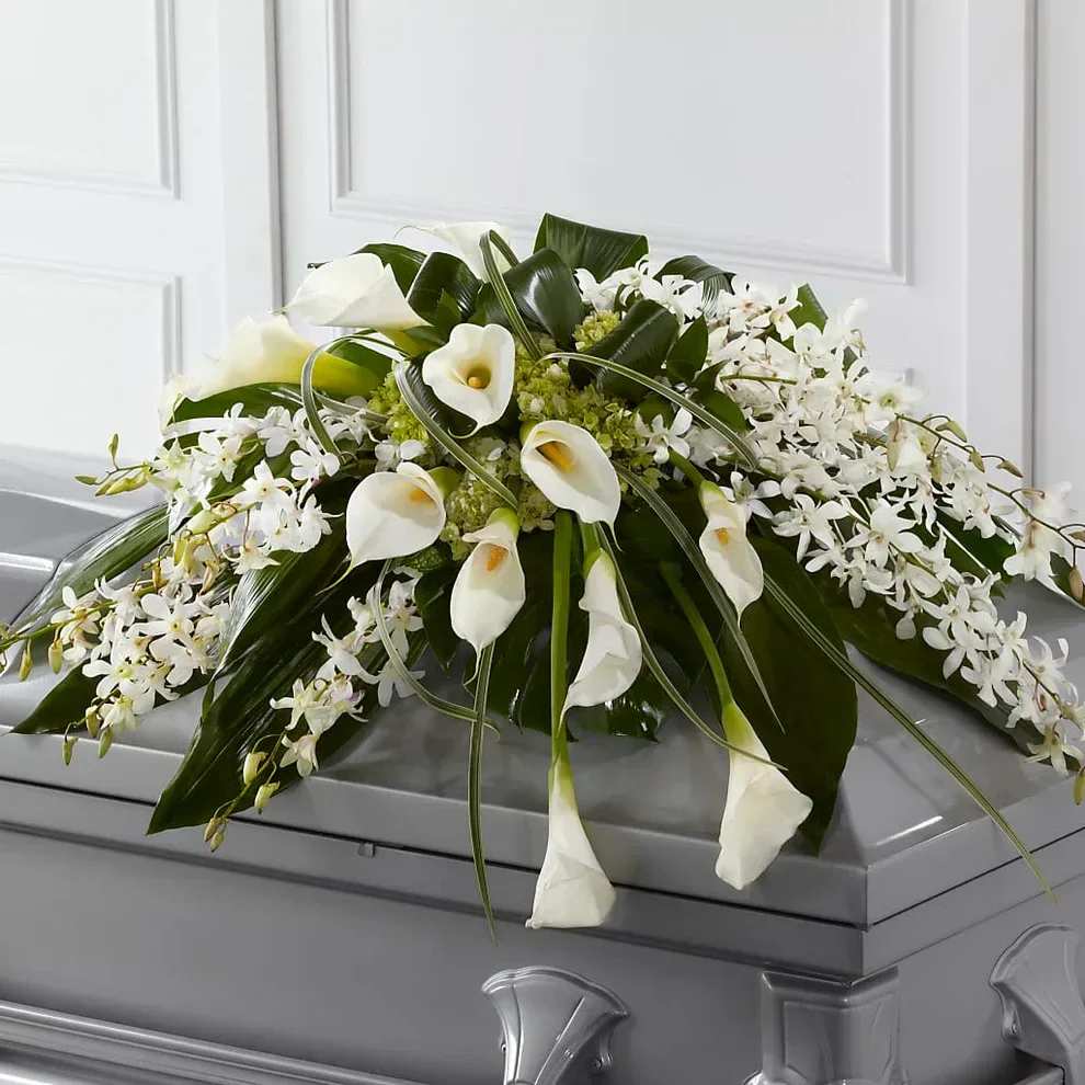 Angel Wings - The Angel Wings Casket Spray is an exceptionally gorgeous way to bring peace and beauty to their final farewell service. White Dendrobium orchids, white calla lilies, green hydrangea and a variety of lush greens are artfully arranged to perfectly adorn the top of their casket, offering the colors and ambience of grace and serenity.