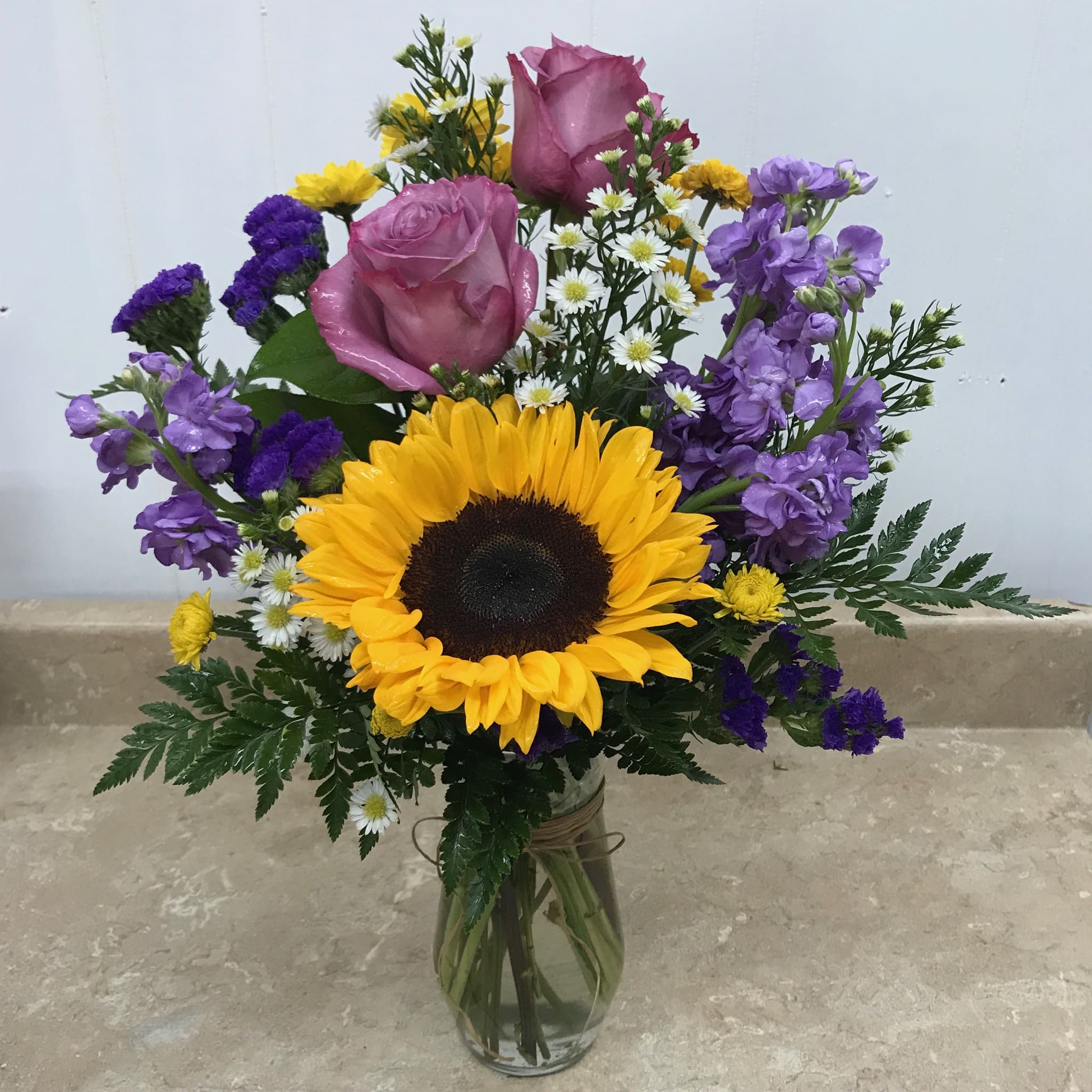 Summer Palette - A colorful combination of bright sunflower, Lavender stock, Lavender roses, yellow chrysanthemum, white monte casino, and purple status. A lovely way to express friendship, love, thanks or just to celebrate!