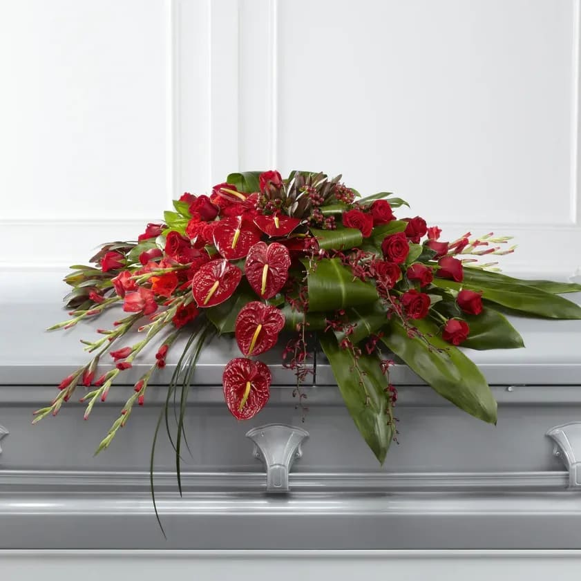 Peaceful Passage - This Peaceful Passage Casket Spray is a graceful way to honor the deceased with tranquil beauty. Brilliant red roses, carnations, gladiolus, anthurium, orchids and hypericum berries are splendidly arranged amongst a variety of lush greens to create the perfect accent piece to bedeck the top of their casket as a moving display of love and affection for their final farewell service.