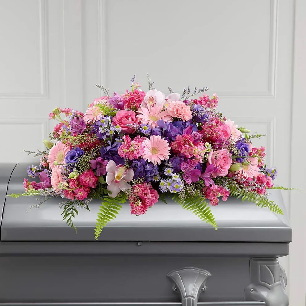 Glorious Garden - Colorful, full and lush, this extraordinary casket spray makes a memorable and touching statement of sympathy that’s sure to be a comfort to grieving family and friends. This vibrant mixed flower casket spray is a generously scaled floral creation of bright and blue spring color, constructed by our talented designers and includes pink carnations, cymbidium orchids and gerbera daisies, hot pink roses and stock, purple hydrangea and lisianthus, lavender alstroemeria, Monte Casino and limonium all accented with lush greens.