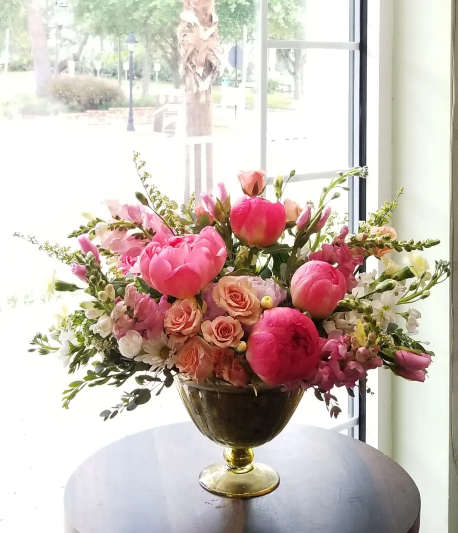 Amélie – Garden Peony Arrangement (May-June) - Seasonal Flower Disclaimer Peonies are a seasonal bloom typically available from May through June. When peonies are not available, they will be thoughtfully substituted with luxurious garden roses or similar premium blooms, while preserving the overall color palette, style, and fullness of the arrangement. *********************************************************************************************** Elegant, romantic, and full of spring charm, Amélie is a luxurious floral design inspired by the beauty of Parisian garden blooms.  This lush arrangement features a romantic palette of vibrant pink peonies, blush roses, soft peach spray roses, and delicate seasonal flowers arranged with airy garden movement. Accents of snapdragons, stock, and fresh greenery create a layered composition that feels abundant, graceful, and full of life.  Designed in a classic gold pedestal vase, the arrangement brings a refined and timeless presence to any space. Vibrant peonies create a striking focal point while soft blush and peach blooms add warmth and balance to the design.  Each arrangement is handcrafted by the designers at ImpeKable Flowers in DeLand using carefully selected seasonal blooms sourced from premium growers.  A beautiful choice for Mother’s Day, birthdays, anniversaries, or celebrating someone truly special.  We proudly offer flower delivery throughout DeLand, Lake Mary, Sanford, Deltona, Orange City, DeBary, Altamonte Springs, and surrounding Central Florida communities.