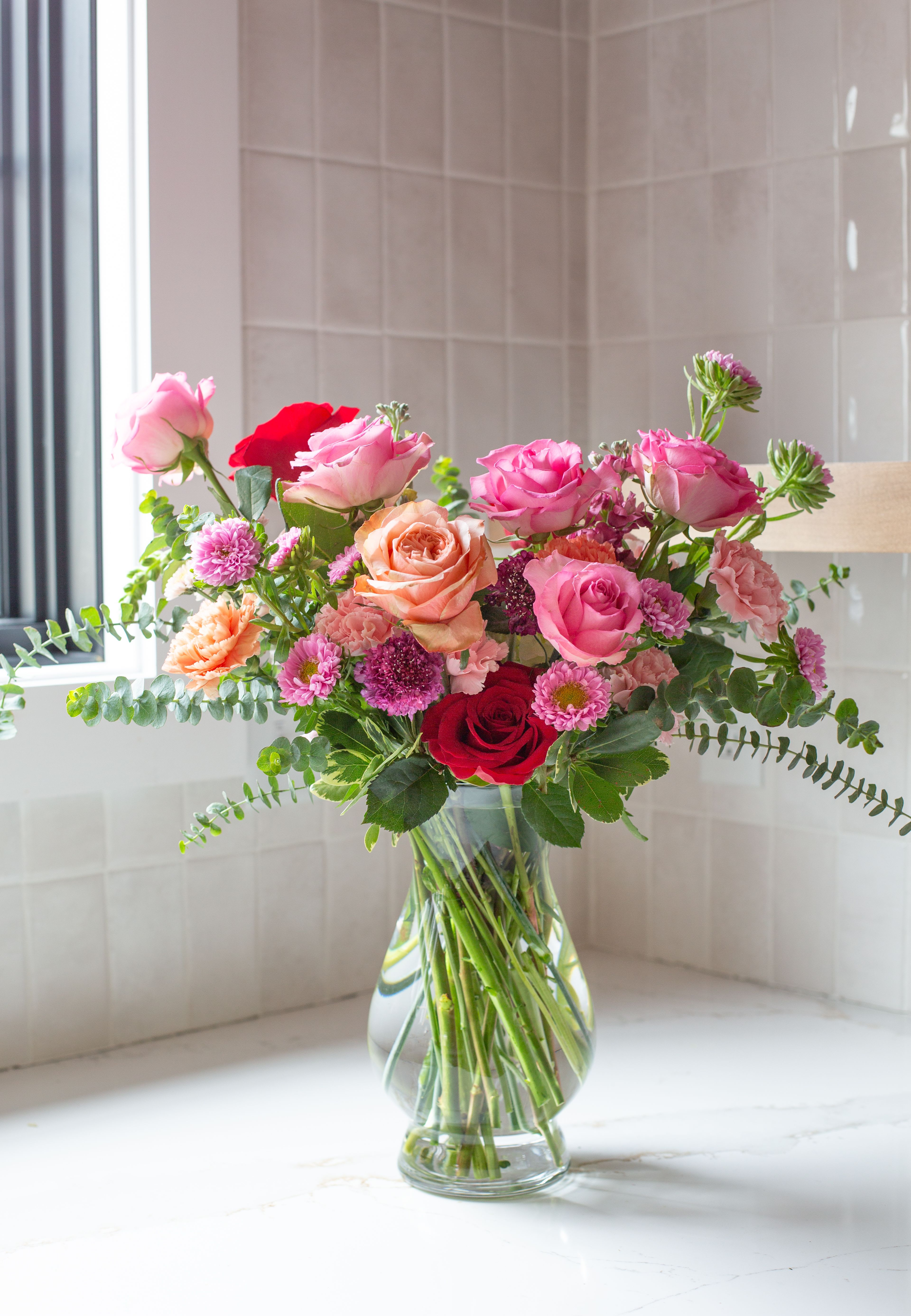 Unforgettable – Classic Garden Rose Arrangement - Elegant, timeless, and full of heartfelt beauty, Unforgettable is a classic garden-style floral arrangement designed to celebrate the people who leave a lasting impression on our lives.  This lush design features a romantic blend of pink, blush, peach, and deep red roses accented with seasonal blooms and fresh greenery. Delicate carnations, chrysanthemums, and airy garden textures create depth and softness, giving the arrangement a naturally abundant feel.  Arranged in a clear glass vase with graceful, airy movement, the flowers create a balanced composition that feels both traditional and fresh. The combination of warm pinks and vibrant reds adds richness and emotion, making the arrangement perfect for meaningful celebrations.  Each piece is handcrafted by the designers at ImpeKable Flowers in DeLand, using carefully selected seasonal blooms sourced from premium growers.  A beautiful choice for Mother’s Day, birthdays, anniversaries, or expressing love and appreciation for someone truly unforgettable.  We proudly offer flower delivery throughout DeLand, Lake Mary, Sanford, Deltona, Orange City, DeBary, Altamonte Springs, and surrounding Central Florida communities.  Flower varieties may vary slightly depending on seasonal availability while maintaining the same color palette and overall design style. 