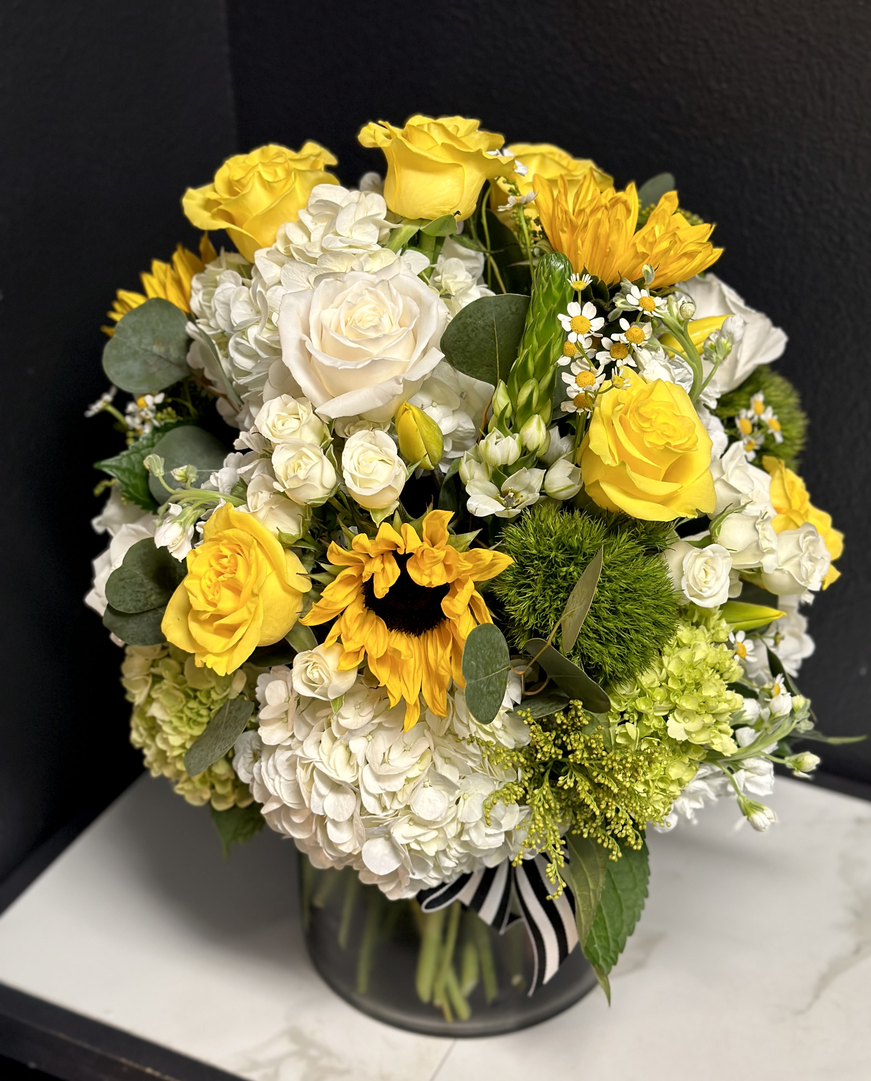 Lavish Sunny Garden - A lavish seasonal arrangement, with our most premium floral varieties in shades of yellow, cream, white, and green. Designed in our signature English Garden style and delivered in a clear glass vase.  Overall design is approximately 16"x16" Floral varieties may vary but will be of similar quality and style.  