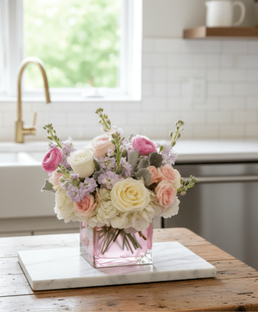 Daniela – Soft Garden Arrangement - Delicate, elegant, and full of gentle beauty, Daniela is a soft garden-style floral arrangement inspired by timeless spring blooms.  This charming design features a romantic palette of blush pink, soft lavender, creamy white, and pale peach flowers. Premium roses, ranunculus, hydrangea, and delicate seasonal blooms are arranged with natural movement and airy texture, creating a composition that feels light, graceful, and effortlessly refined.  Designed in a modern blush glass cube vase, the arrangement brings a soft and sophisticated presence to any home. The pastel tones create a calming and uplifting atmosphere, making it a beautiful gift for meaningful moments.  Each arrangement is handcrafted by the designers at ImpeKable Flowers in DeLand, using carefully selected seasonal flowers sourced from premium growers.  A lovely choice for Mother’s Day, birthdays, baby celebrations, thank-you gifts, or simply brightening someone’s day.  We proudly offer flower delivery throughout DeLand, Lake Mary, Sanford, Deltona, Orange City, DeBary, Altamonte Springs, and surrounding Central Florida communities.  Flower varieties may vary slightly depending on seasonal availability while maintaining the same color palette and overall design style
