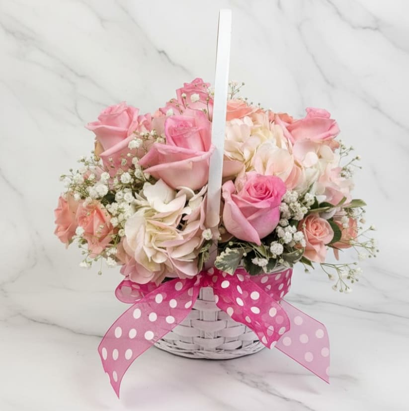 Blushing Garden Basket - A soft and romantic basket arrangement featuring blush and pink roses, creamy hydrangea, peach spray roses, and delicate baby’s breath. Designed in a white woven basket and finished with a playful pink polka-dot ribbon, this sweet arrangement is perfect for welcoming a new baby, celebrating spring, or sending a heartfelt surprise.
