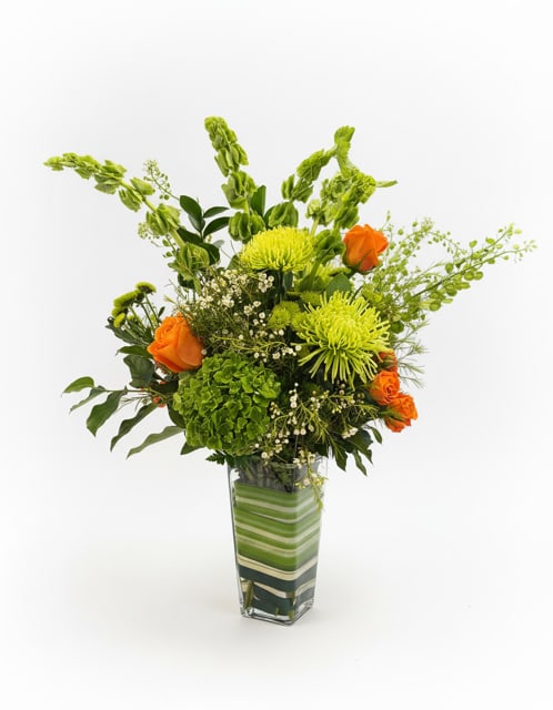 Citrus Garden Luxe - A lush, large-scale arrangement bursting with vibrant green textures and bright orange roses. Featuring hydrangea, spider mums, snapdragons, and seasonal accents, this striking design is arranged in a modern glass vase with layered greenery for an elevated look. Full of height, texture, and fresh color, this statement arrangement makes a bold impression for celebrations, birthdays, or sending something truly special.