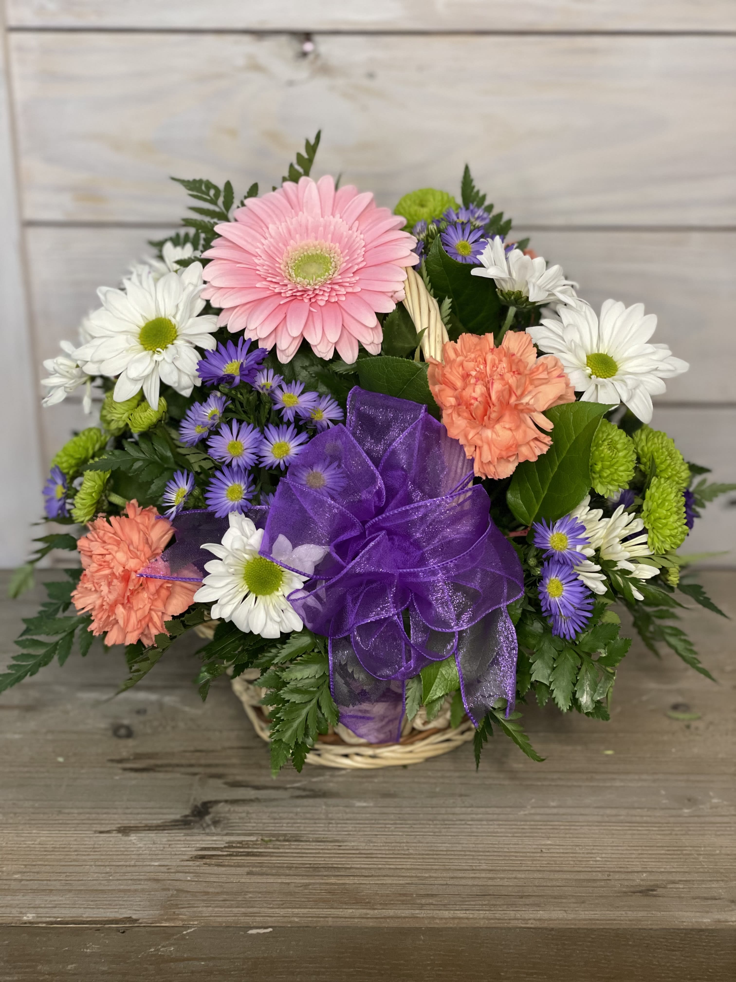 Mixed bouquet of daisies, gerbera, and carnations in a basket with a purple bow