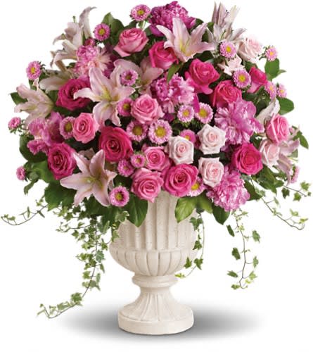 Pink roses and lilies arranged in a white urn vase