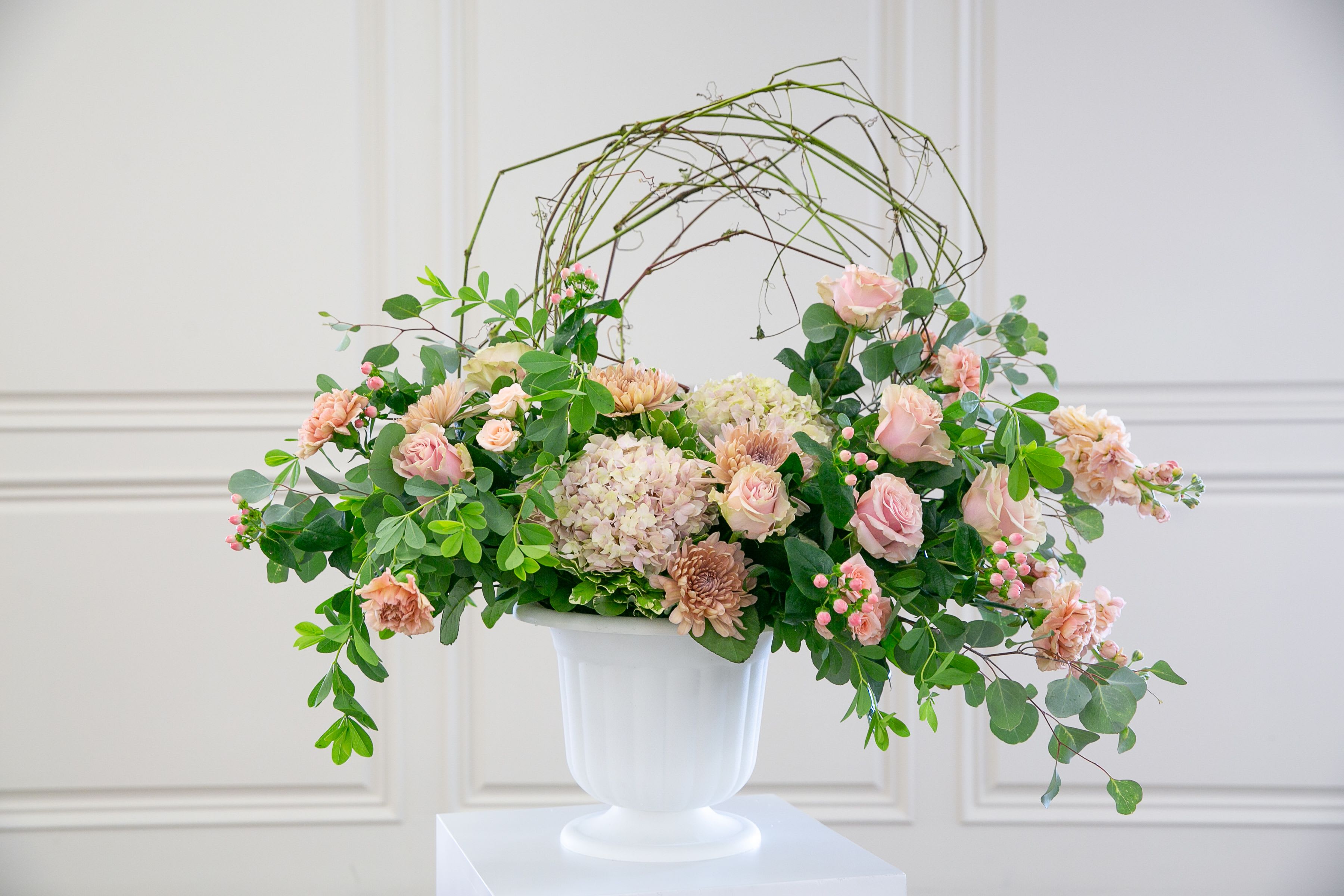 Blush Garden Tribute   - Soft, graceful, and filled with quiet beauty, Blush Garden Tribute is a floral arrangement designed to offer comfort and remembrance during life’s most tender moments.  This elegant design features a gentle palette of blush roses, soft carnations, hydrangea, and seasonal blooms layered with fresh greenery and delicate textural accents. Natural branches form a subtle halo above the flowers, creating a symbolic circle that represents eternity, memory, and enduring love.  Designed in a classic white pedestal vase, the arrangement has an airy garden style with natural movement and soft cascading greenery. The gentle blush tones create a peaceful presence while the organic structure adds depth and quiet elegance to the tribute.  Each arrangement is handcrafted by the designers at ImpeKable Flowers in DeLand, using carefully selected seasonal blooms sourced from premium growers.  A meaningful floral expression for memorial services, celebration-of-life gatherings, or sending sympathy to loved ones.  Flower varieties may vary depending on seasonal availability while maintaining the same color palette and overall design style.