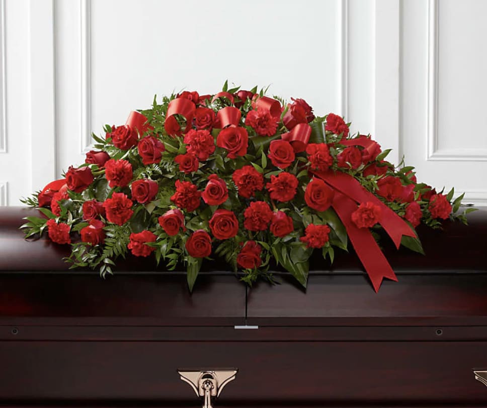Red rose and carnation casket spray with ribbon on a dark casket