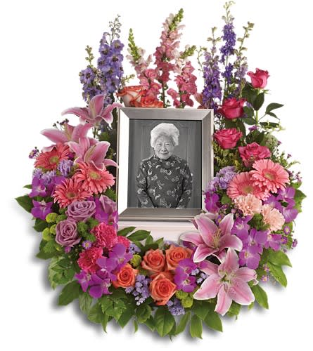 In Memoriam Wreath T253-1A - Devotion is expressed and beautiful memories cherished with this deep-hued and softly elegant wreath. A lovely reminder of your affection and respect. A mix of dramatic flowers such as purple orchids and asters orange dark pink and lavender roses pink and peach carnations lavender larkspur green chrysanthemums and a range of pink blooms including oriental lilies gerberas snapdragons and more. Please note: Arrangement does not include picture frame.Approximately 26" W x 31" H Orientation: One-Sided As Shown : T253-1A