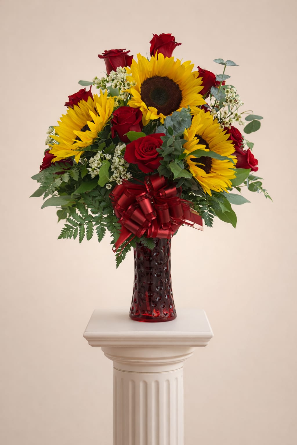 Tall arrangement of yellow sunflowers and red roses in a red glass vase with a red bow.