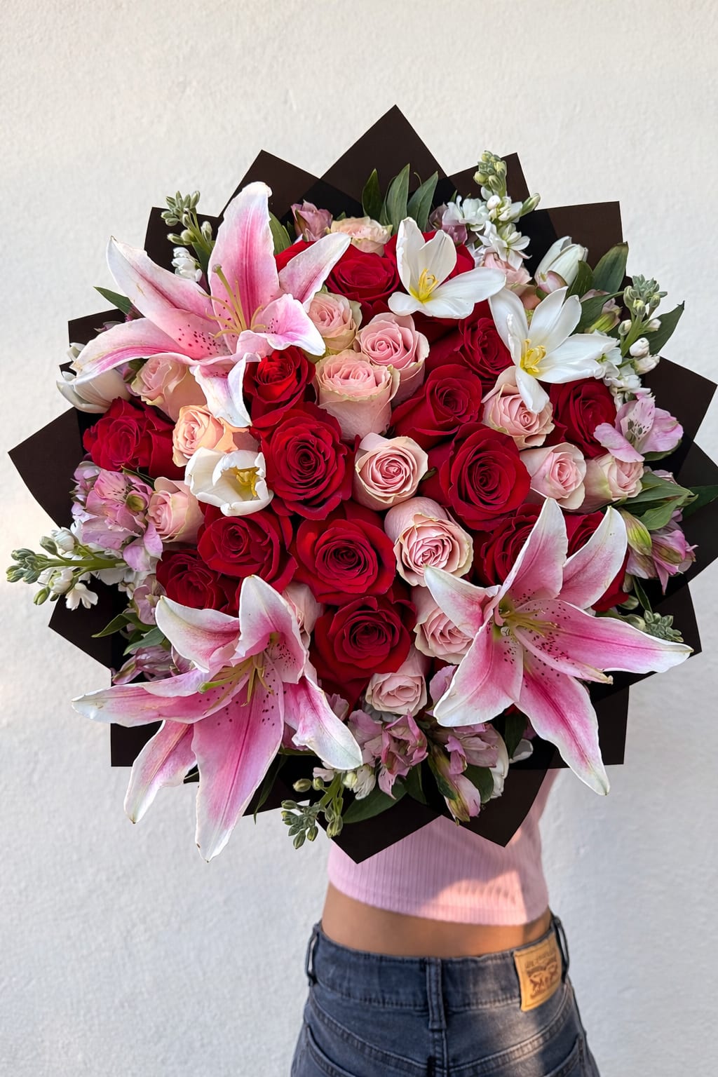 Blushing Romance Bouquet - A breathtaking bouquet designed to make a lasting impression. This luxurious  arrangement features a stunning blend of 18 velvety red roses, 18 soft blush roses and elegant pink lilies, accented with delicate season blooms and a lush green wrapped in modern black paper for a dramatic and sophisticated finish. This book creates the perfect balance of romance and elegance.