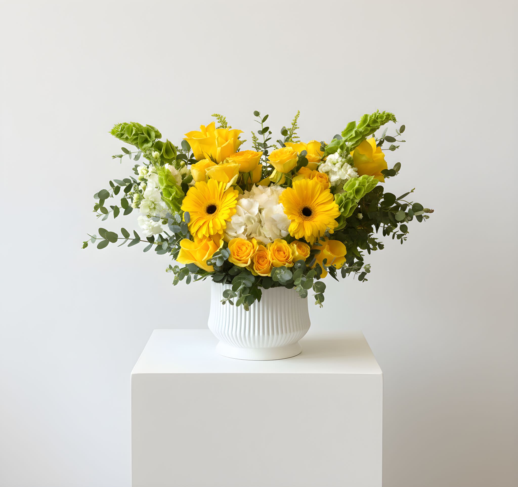 Golden Sunshine Yellow Roses &amp; Gerbera Arrangement - Brighten any space with our Golden Sunshine Yellow Roses &amp; Gerbera Arrangement, a vibrant and uplifting design that radiates warmth and happiness. This beautiful arrangement features a stunning mix of yellow roses, cheerful gerbera daisies, delicate hydrangeas, and seasonal accent blooms, complemented by fresh greenery for a natural and balanced look.  Designed in a modern white ceramic vase, this arrangement is perfect for birthdays, celebrations, thank-you gifts, housewarmings, or simply bringing a touch of sunshine into someone’s day. The bright yellow tones symbolize joy, friendship, and positivity, making it a thoughtful gift for many occasions.  Each arrangement is handcrafted with care to ensure a full, fresh, and elegant presentation.  Please note: Flower varieties and shades may vary slightly depending on seasonal availability while maintaining the overall color palette and design style of the arrangement.