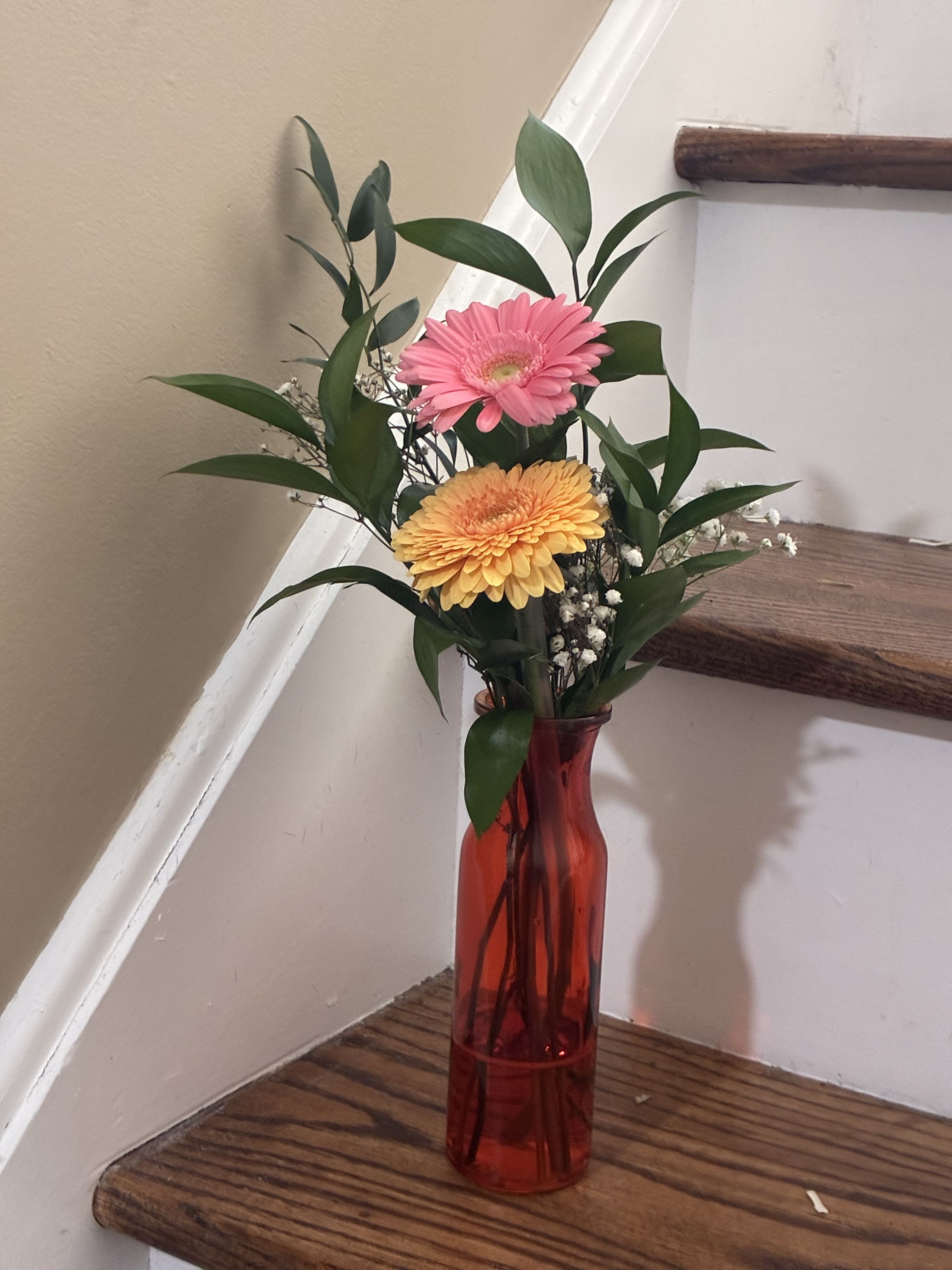 Gerber Baby - Two cheerful gerbera daisies arranged in a simple bud vase for a bright and playful pop of color. Known for their bold centers and vibrant petals, gerberas bring instant happiness to any space. This petite floral design is perfect for desks, small tables, or sending a little burst of joy.