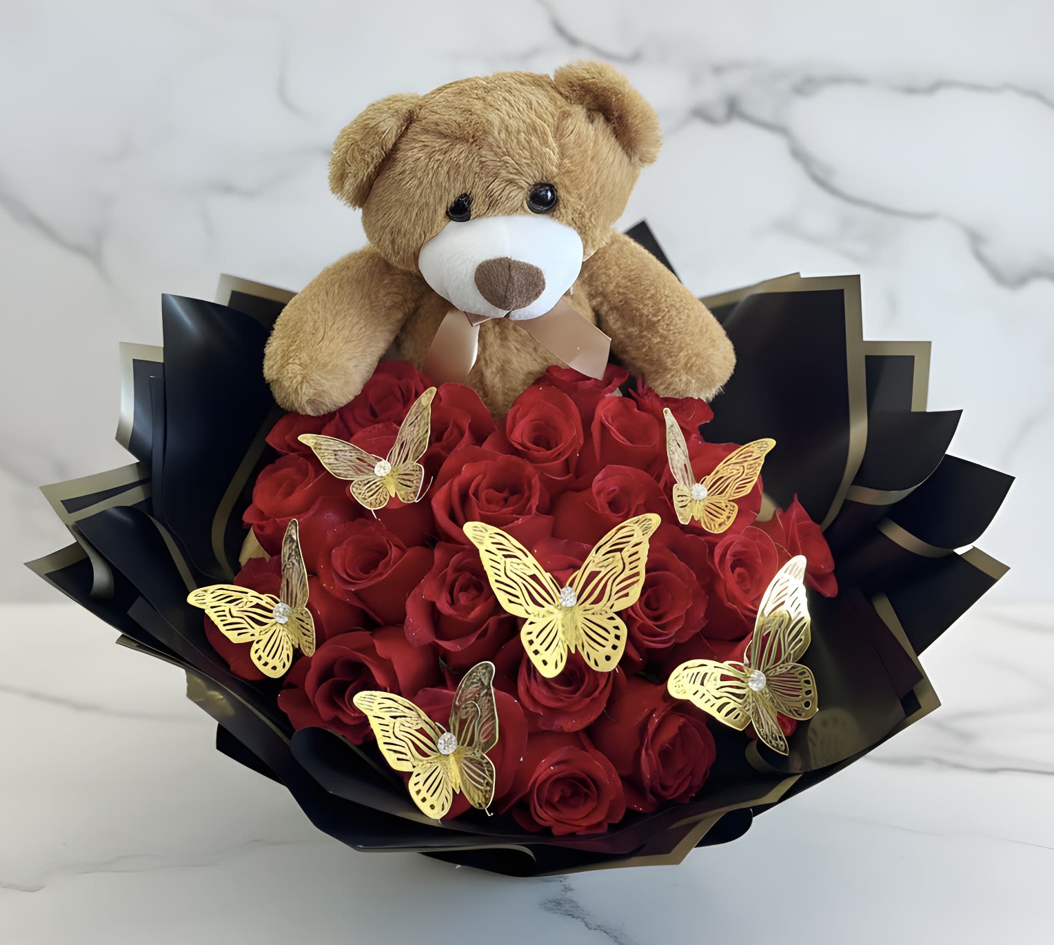 Teddy bear sitting on a bouquet of red roses with gold butterfly decorations