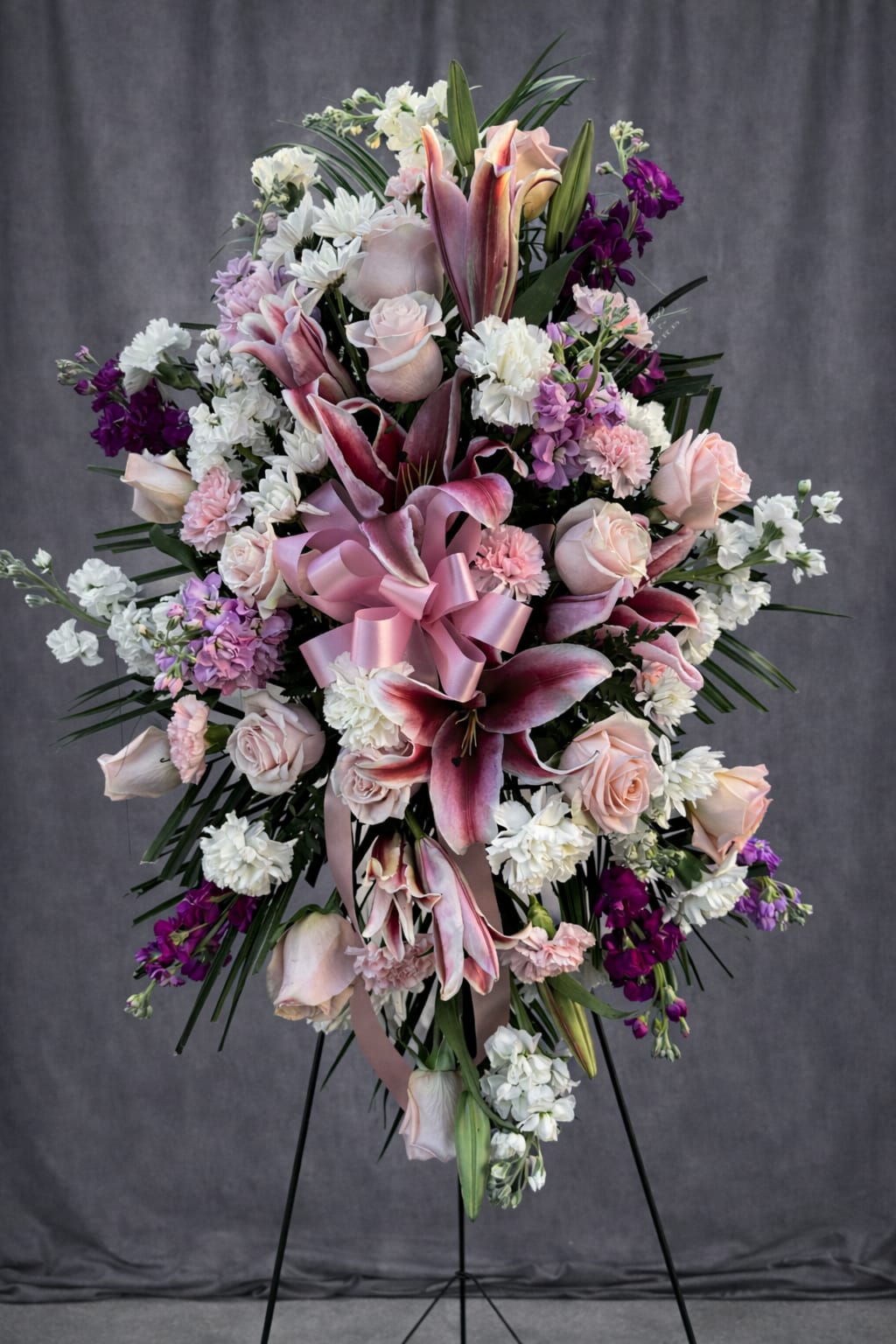 Graceful Farewell - The soft blush roses, stargazer lilies, and layers of pinks, whites, and purples give it an elegant yet tender presence. The overall design radiates love, remembrance, and serenity—perfect for honoring someone cherished.