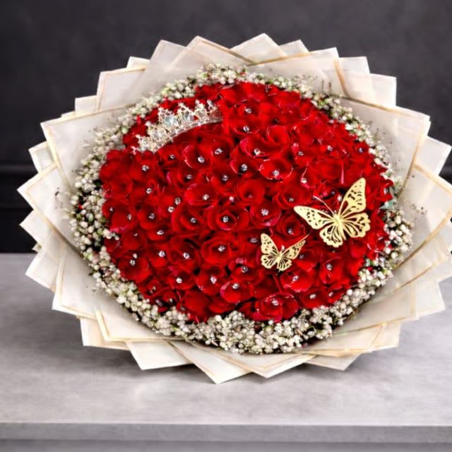 Ramo Buchon  - Elegant bouquet wrapped in decorative paper, featuring 100 red roses, each adorned with a sparkling diamond accent. Includes 3 delicate butterflies and a beautifully coordinated bow for a luxurious, romantic finish.  Trim the Stems: Cut approximately 2cm off the bottom of each stem at a 45-degree angle. This allows for maximum water absorption.  Hydrate Immediately: Place the roses in a clean vase filled with fresh, room-temperature water.  Clean the Water: Ensure no leaves are submerged below the water line, as this can cause bacteria to grow.  Stay Cool: Keep your bouquet in a cool spot away from direct sunlight, heaters, or ripening fruit.   