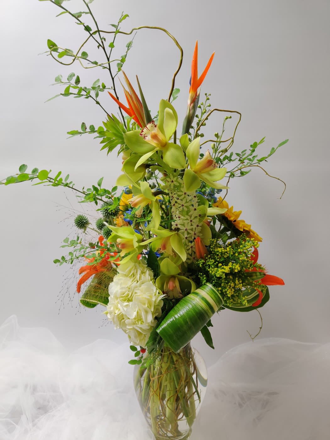 Modern Tropical Flowers - This arrangement has Birds of Paradise, Cymbidium, Hydrangea, Pineapple, Lily, Solidago, Thistle, and tropical greenery in a tall vase