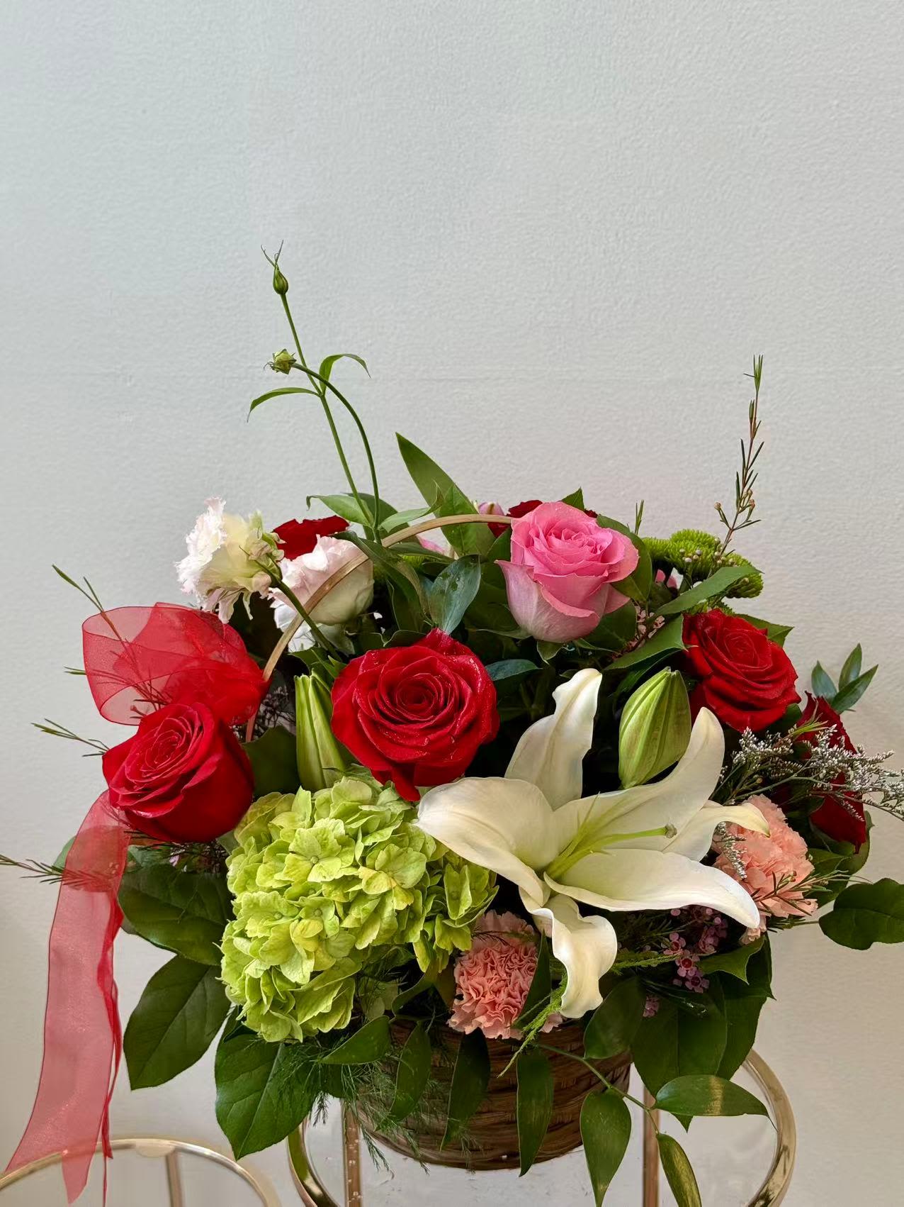 Sweetheart Bloom Basket - A romantic garden-style basket featuring vibrant roses, elegant lilies, and soft seasonal blooms, accented with lush greenery. Hand-designed to create a warm and joyful floral gift for any occasion.