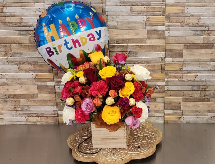 Celebrating with roses and ferrero -Celebrando con rosas y ferrero - Celebrate their special day with this cheerful floral arrangement in a modern wooden box, featuring a vibrant mix of premium roses, fresh carnations, seasonal blooms, and lush greenery. Accented with delicious Ferrero Rocher chocolates and topped with a festive Happy Birthday balloon, this joyful design is the perfect all-in-one gift to surprise and delight anyone on their birthday. 