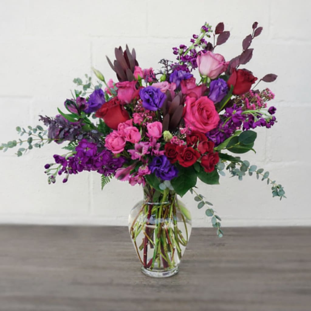 Love Bomb - A bold mix of vibrant roses and rich purple blooms designed to make a statement. Love Bomb is a lush, eye-catching arrangement that says everything—without saying a word