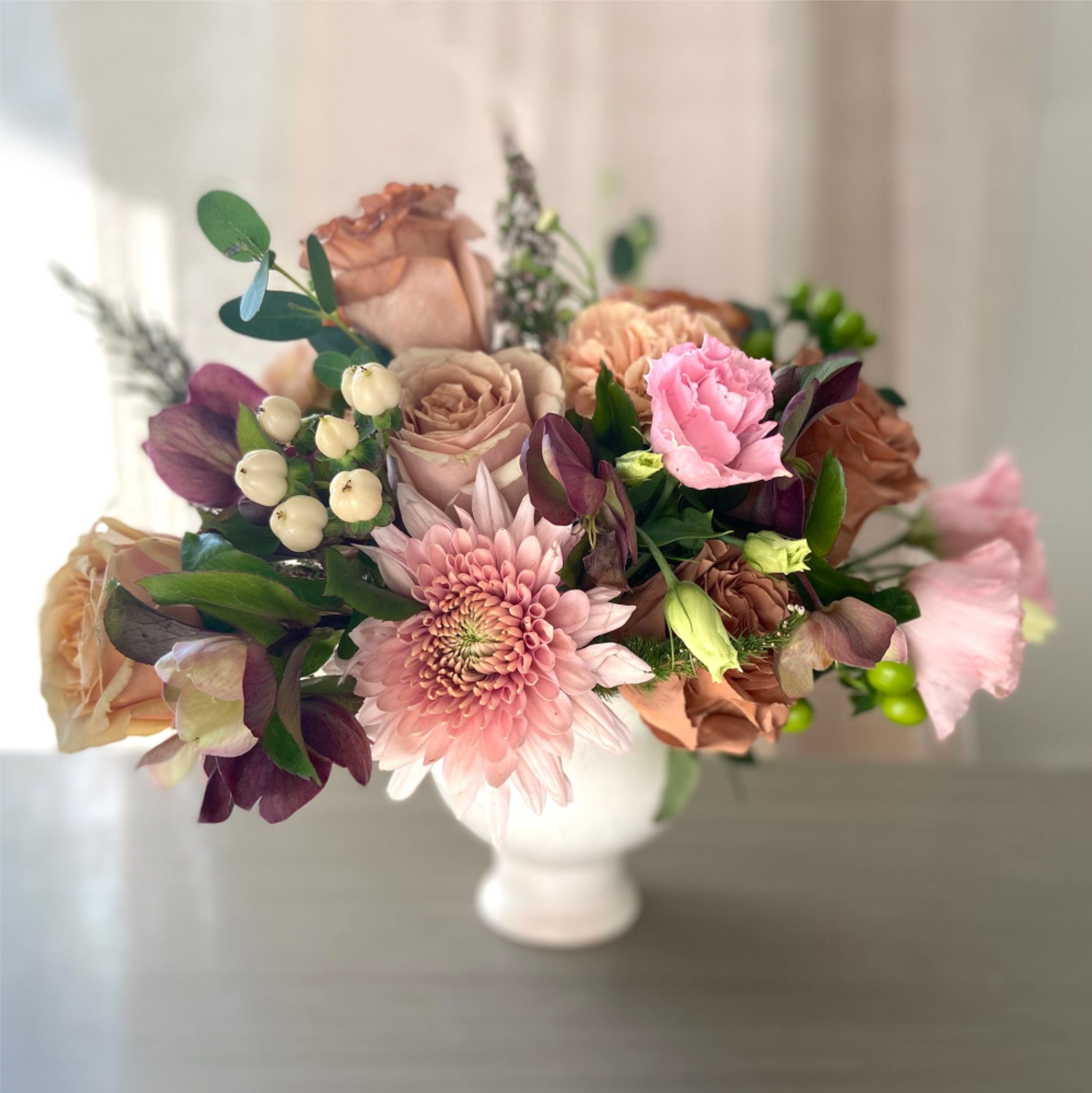 Desert Rose - A soft, sun-washed arrangement featuring blush and camel garden roses, rich-toned hellebore, and gentle pops of seasonal greenery.  Designed with an airy hand and a neutral-leaning palette, it’s warm, refined, and effortlessly elegant—perfect for a thoughtful gesture or a quiet moment of beauty.