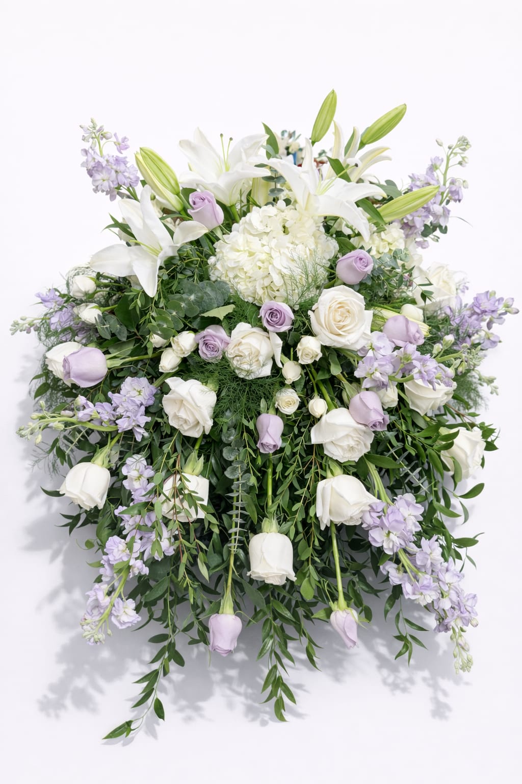 Garden Centerpiece - Elegant, romantic, and designed to capture the beauty of a wedding day, this breathtaking centerpiece is perfect for the sweetheart table or the head table of the bride and groom. A luxurious blend of white lilies, hydrangeas, and roses is delicately accented with soft lavender blooms and lush cascading greenery.  The gentle mix of white and lavender tones symbolizes purity, love, and new beginnings, creating a refined and dreamy atmosphere for one of the most special tables of the celebration.  With its graceful garden-inspired design and flowing greenery, this arrangement brings softness, elegance, and romance to the heart of the wedding reception.  A stunning floral statement created to celebrate love.