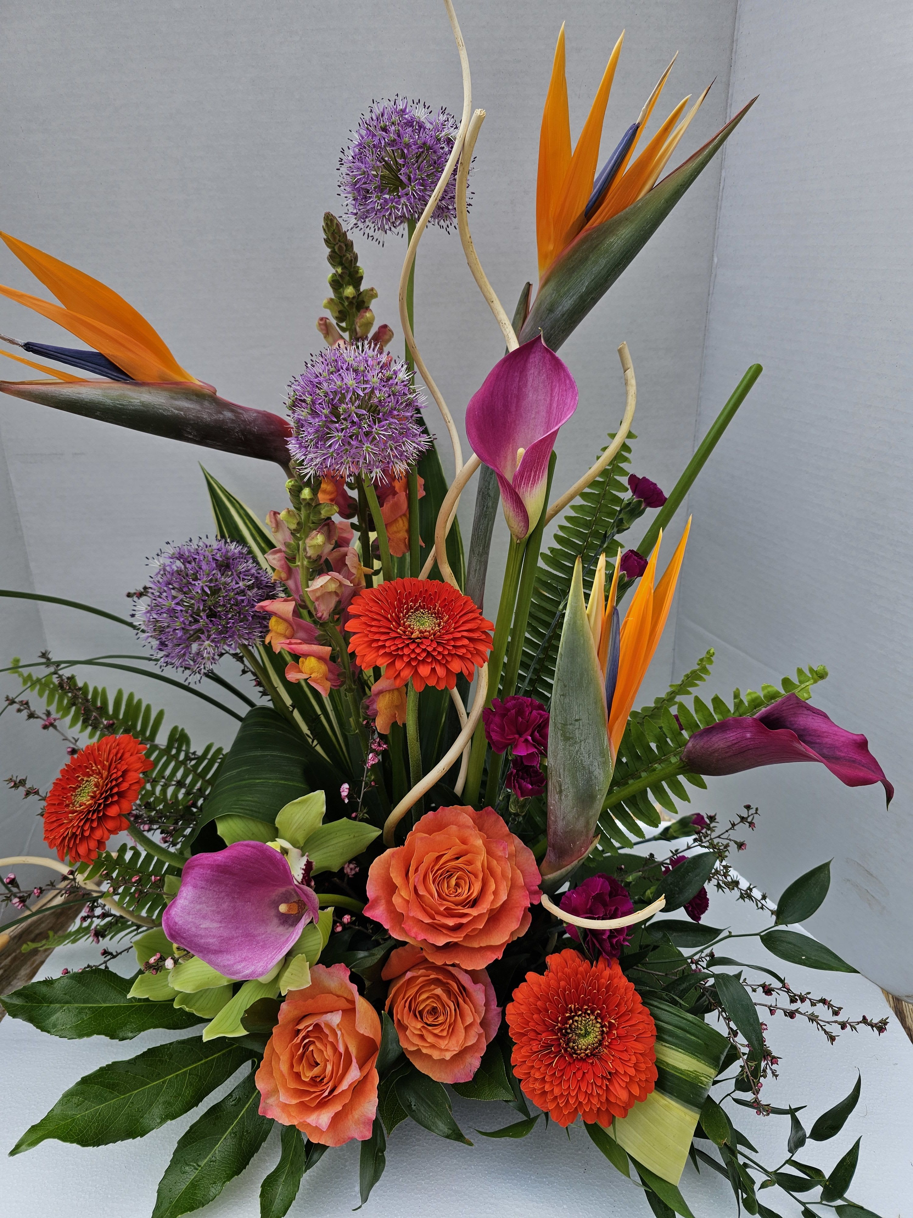 Tropical paradise - Modern arrangement using bird of paradise, cala lily,orange roses and allium.