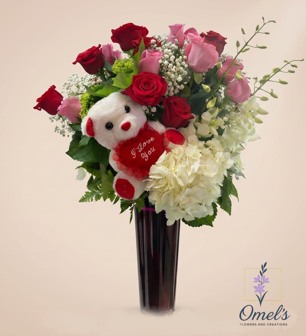 Bear and Booms - Let this charming arrangement speak from the heart when words aren't enough. Bear and Blooms is a sophisticated yet sweet expression of affection, featuring a lush and vibrant mixture of deep red and soft pink roses, interwoven with delicate sprigs of baby's breath and a substantial cluster of white hydrangeas. The blooms are nestled in a unique, deep purple-tinted glass vase with a chic matte finish, giving the whole piece a modern and elegant feel. But the highlight of this heartfelt creation is the adorable white plush teddy bear, complete with festive red paws, holding a matching red heart that says "I Love You" in delicate cursive script. It’s the perfect, unforgettable way to send a message of love and comfort. Ideal Occasions: Valentine's Day, an anniversary, a first date, to say "Thinking of You," a sweet gesture to cheer someone up, or even for a new baby celebration (as a very sweet new mom gift).