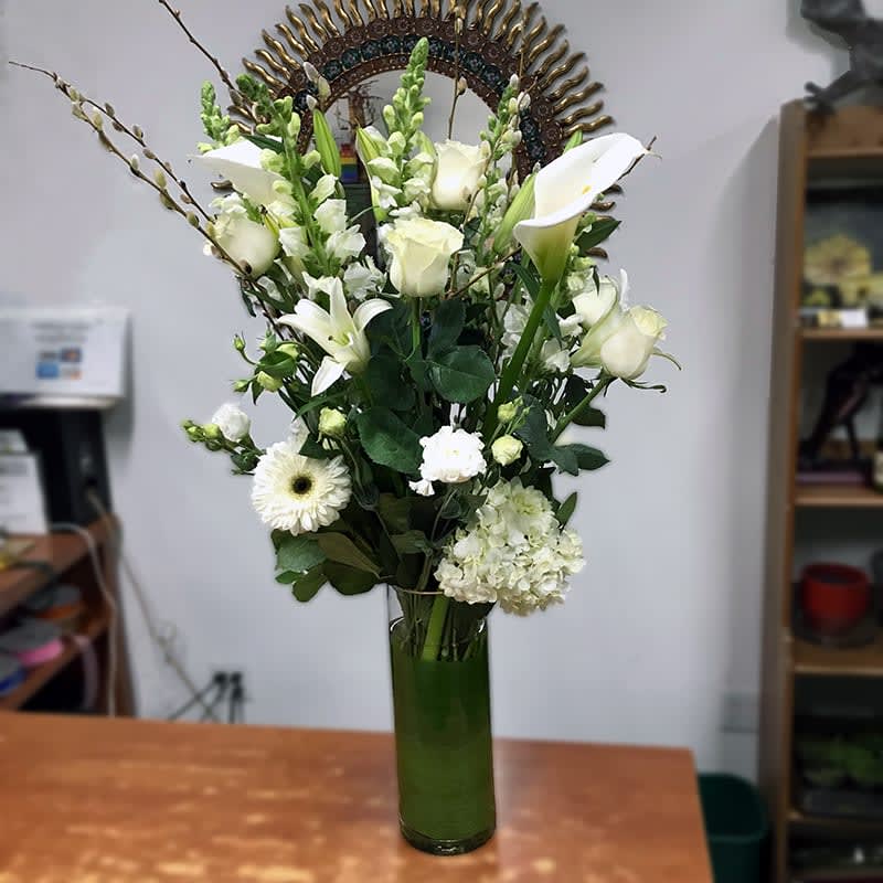White Snow  - Exclusive design from our Brooklyn studio. White calla lilies, roses, snapdragons, lisianthus, gerbera daisy, and hydrangeas. The bouquet arranged in a leaf-line glass cylinder vase. Orientation: One-sided.