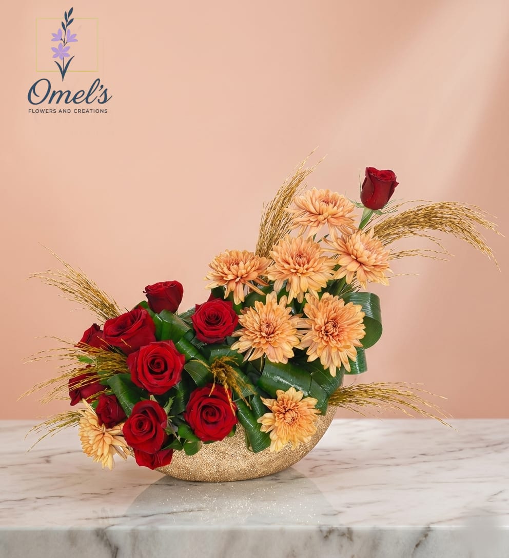Golden Harmony - Crafted for those seeking a modern yet romantic design, it perfectly balances rich color with natural texture, creating a sophisticated feel to make a memorable impression.  Large-headed chrysanthemums in a warm golden-peach hue offer a stunning and soft contrast with classic beaty and passion provided by the vibrant focal point of red roses. Wisps of delicate golden preserved grass add texture, height, and a natural, airy quality to the design. Interwoven loops of large green leaves add depth and a structured, contemporary element.  Set in a elegant, textured golden-glittered container, adding an exquisite sparkle and touch of glamour that elevates the entire presentation,   It is ideal for a romantic gesture or anniversary gift; to celebrate a birthday with unique elegance; for a stylish and thoughtful expression of gratitude; for a distinctive centerpiece for festive gatherings or galas; or for a stunning "just because" sentiment 
