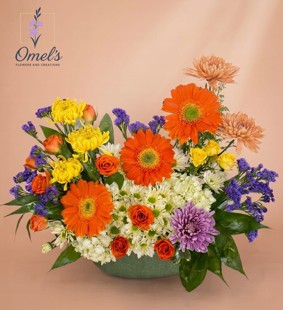 Sunset Symphony - Embrace the warmth of a sunset in full bloom with our joyful, hand-designed bouquet that features a vibrant mix of orange Gerbera Daisies and elegant coral Chrysanthemums, sunny yellow Pompon Mums, golden yellow Spray Roses, delicate white Cushion Mums and pure White Spray Roses, a charming cluster of small Peach-Orange Spray Roses, a unique focal Lavender Spider Mum and clusters of deep purple Statice and lush green foliage for natural contrast and a pop of coolness.  Nestled in a low, textured sage-green ceramic vessel, this low-profile, multi-sided arrangement is a beautiful expression of joy and light.  Ideal for birthday wishes and cheerful greetings, a thoughtful thank-you gift, brightening up a work desk or side table, bringing a touch of sunny color to a celebration or any occasion when you want to send a burst of pure, radiant happiness."