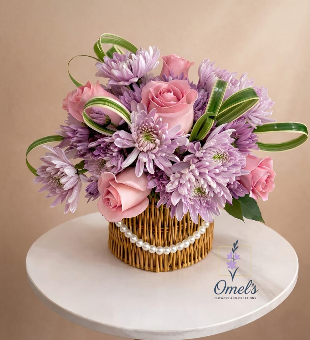 Sweet Charm - A delicate floral design full of tenderness presented in a woven basket adorned with pearls.  It combines soft pink roses with lavender chrysanthemums, creating a harmonious blend of romantic and elegant colors. Decorative greenery form modern curves which adds movement and style to this design conveying sweetness, elegance, and sophistication. Perfect for birthdays, special celebrations, or just to brighten our loved ones' days.