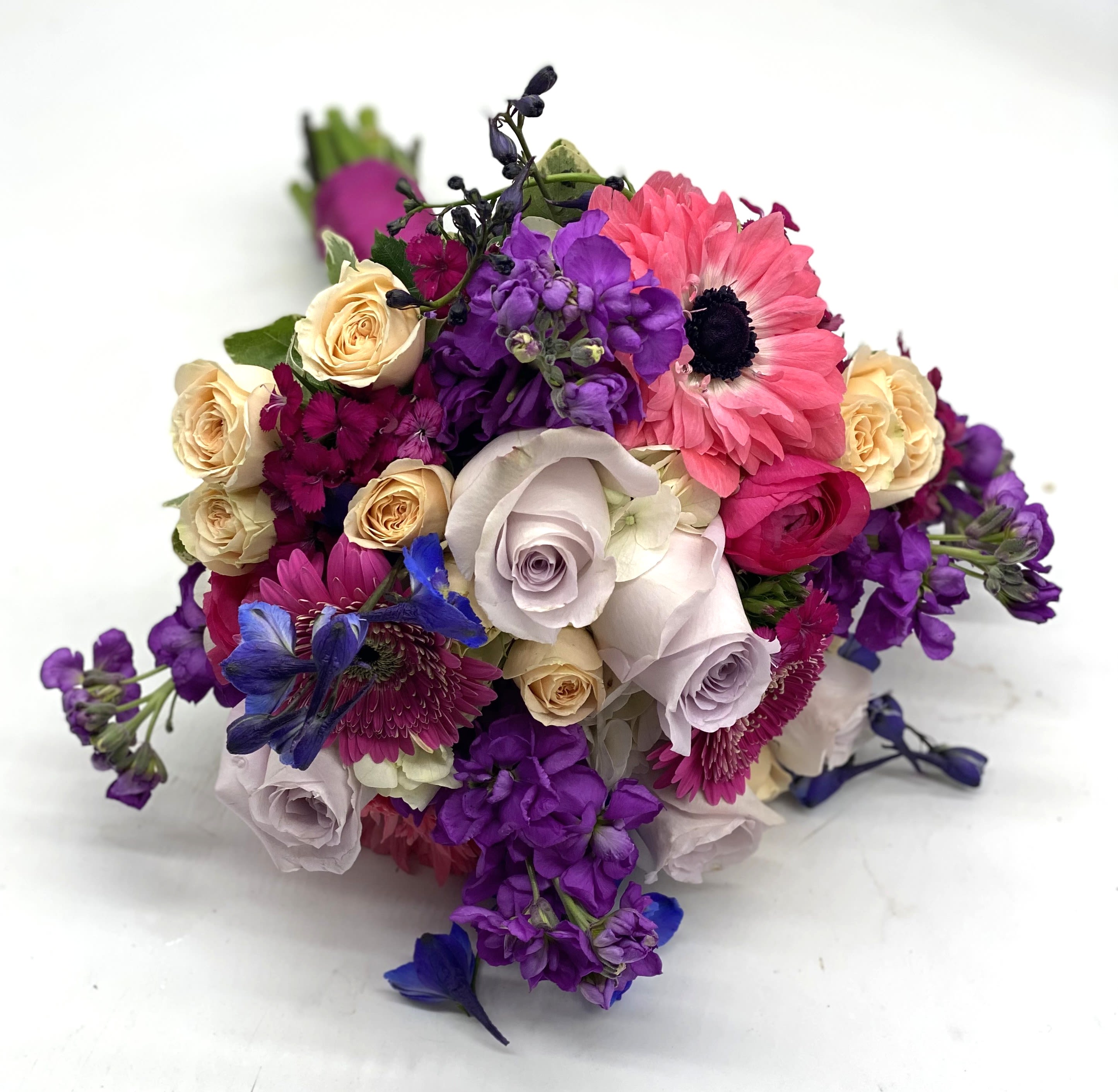 Hand-tied bouquet of purple stock, pink gerbera daisies, roses, and blue delphinium.