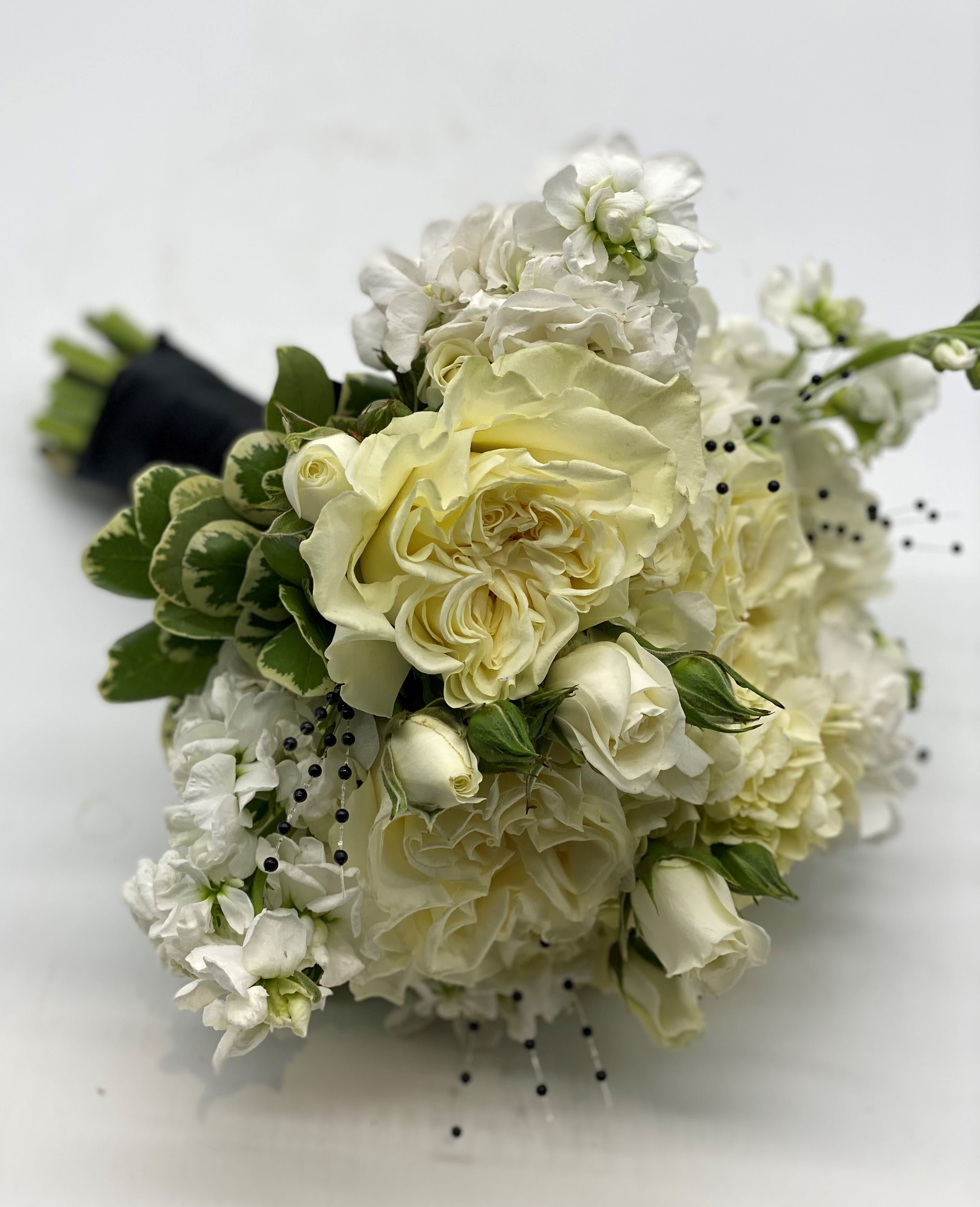 Hand-tied bouquet of ivory roses and white flowers with black bead accents and wrapped stems