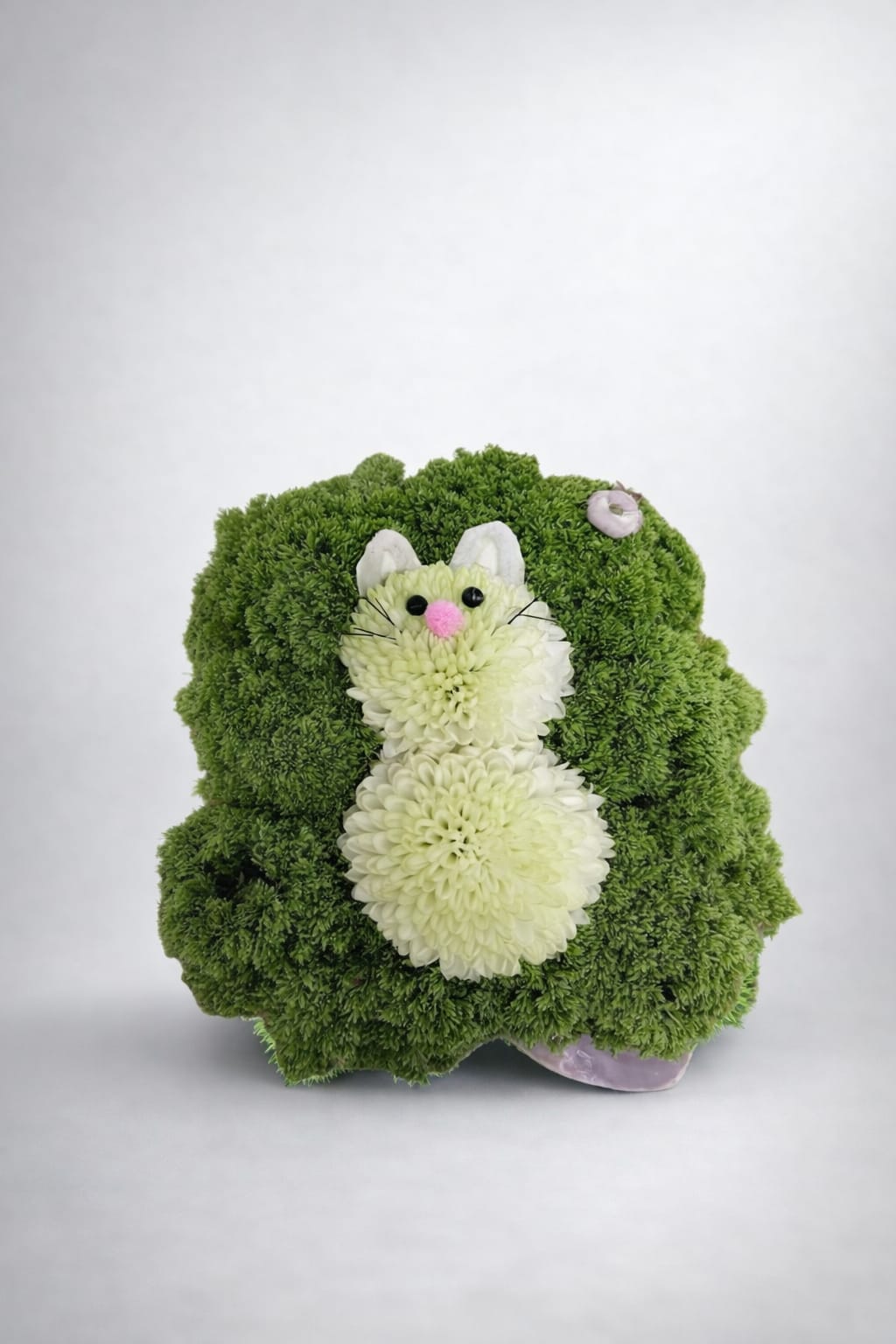 Cheerful Critter Cubes - This delightful arrangement features a charming glass cube filled with vibrant greenery, where a cute critter finds its cozy spot. The blend of trichillium and poms offers a refreshing and enchanting display, making it an ideal choice to brighten up any environment. Whether you're celebrating a birthday or sending well wishes, this wonderful piece is guaranteed to spread happiness and warmth.  When you request custom designs, we will create them to closely resemble the picture. Keep in mind that each design is unique and made just for you. Due to the nature of flowers, color substitutions may be required. Prices and availability of seasonal flowers can also differ.